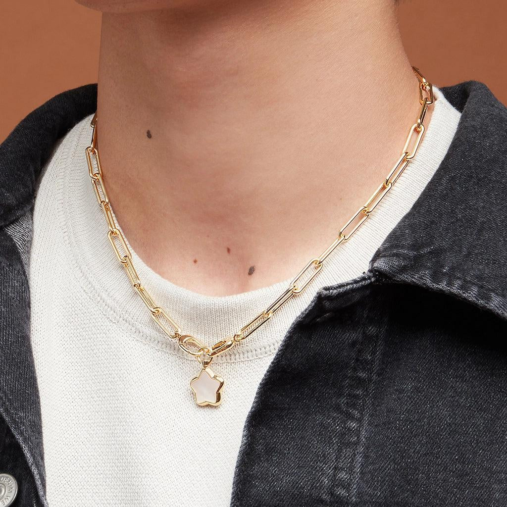 Gold paperclip chain necklace with star charm layered over white crewneck.