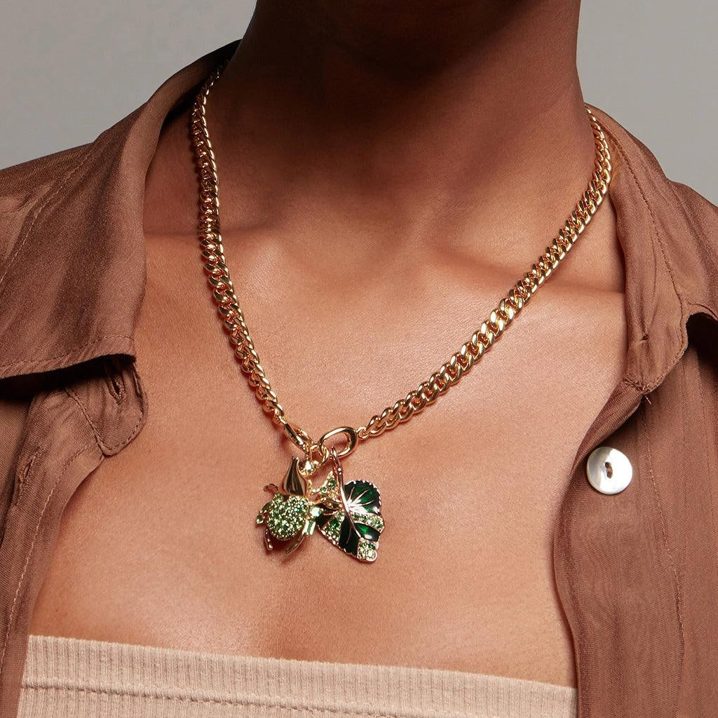 Model wearing a chunky gold chain necklace with green insect and leaf charms