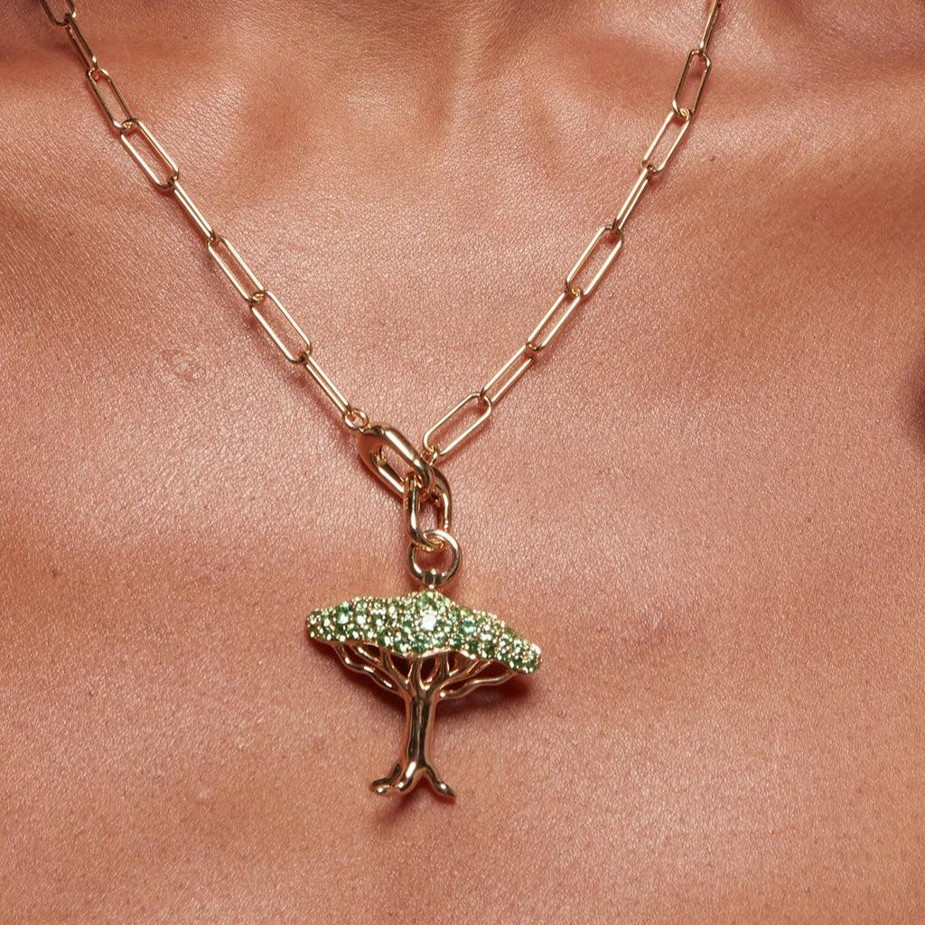Gold chain necklace with green gemstone tree pendant resting on chest.