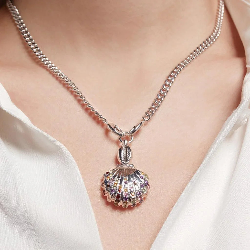 Silver shell charm necklace with multicolor gemstone detailing worn on a white blouse