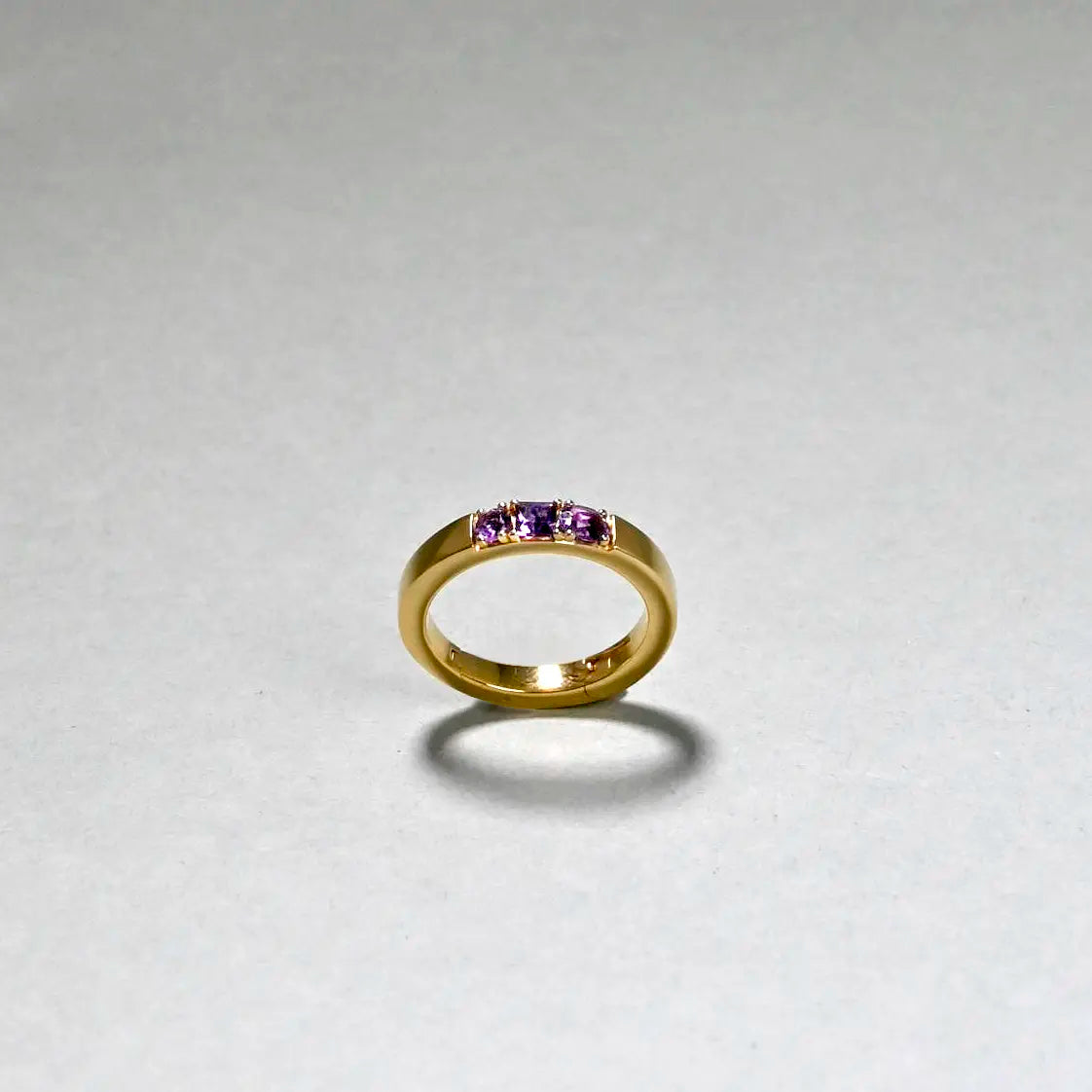 Gold ring with purple gemstones on a light gray background