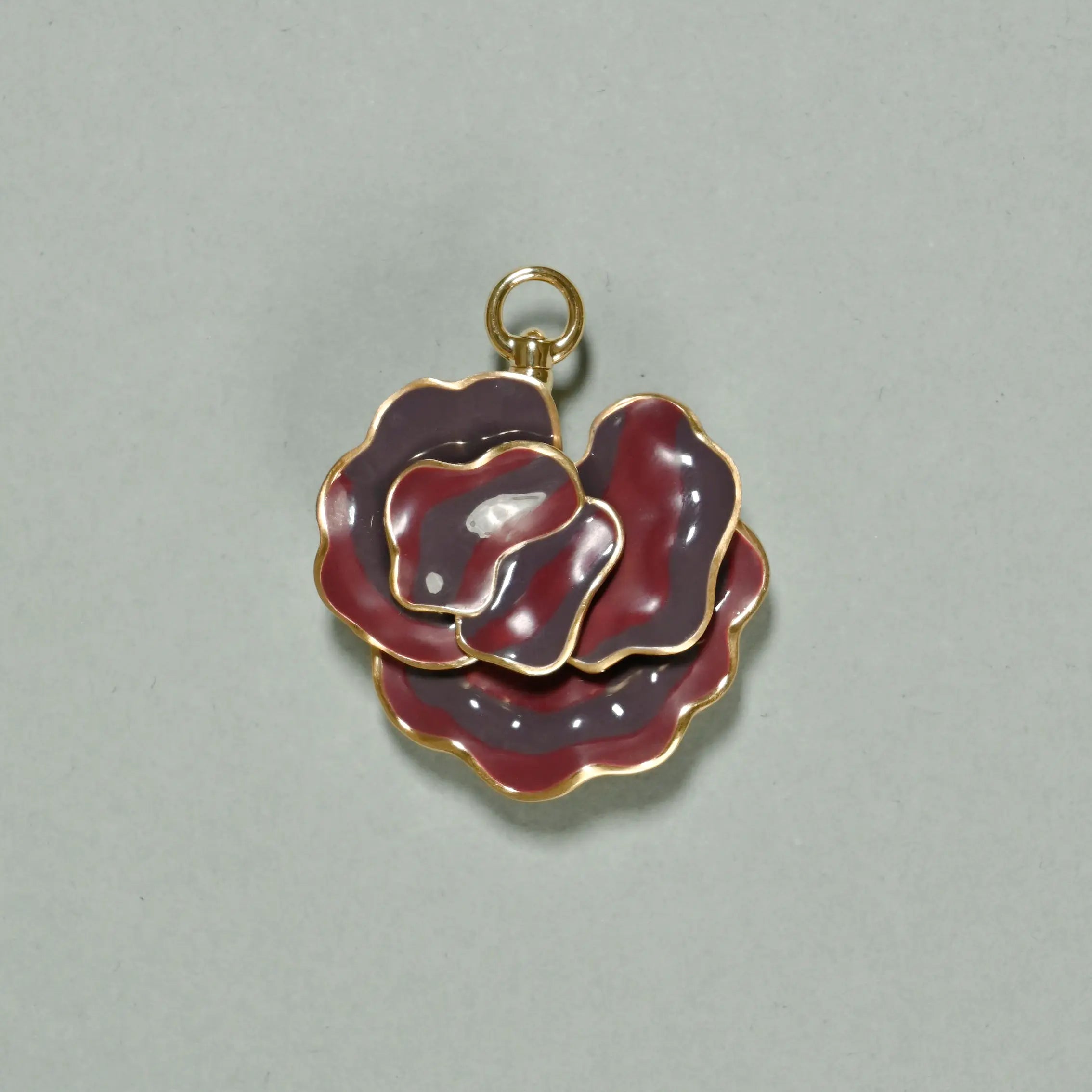 Gold and red enamel rose-shaped pendant on a gray background