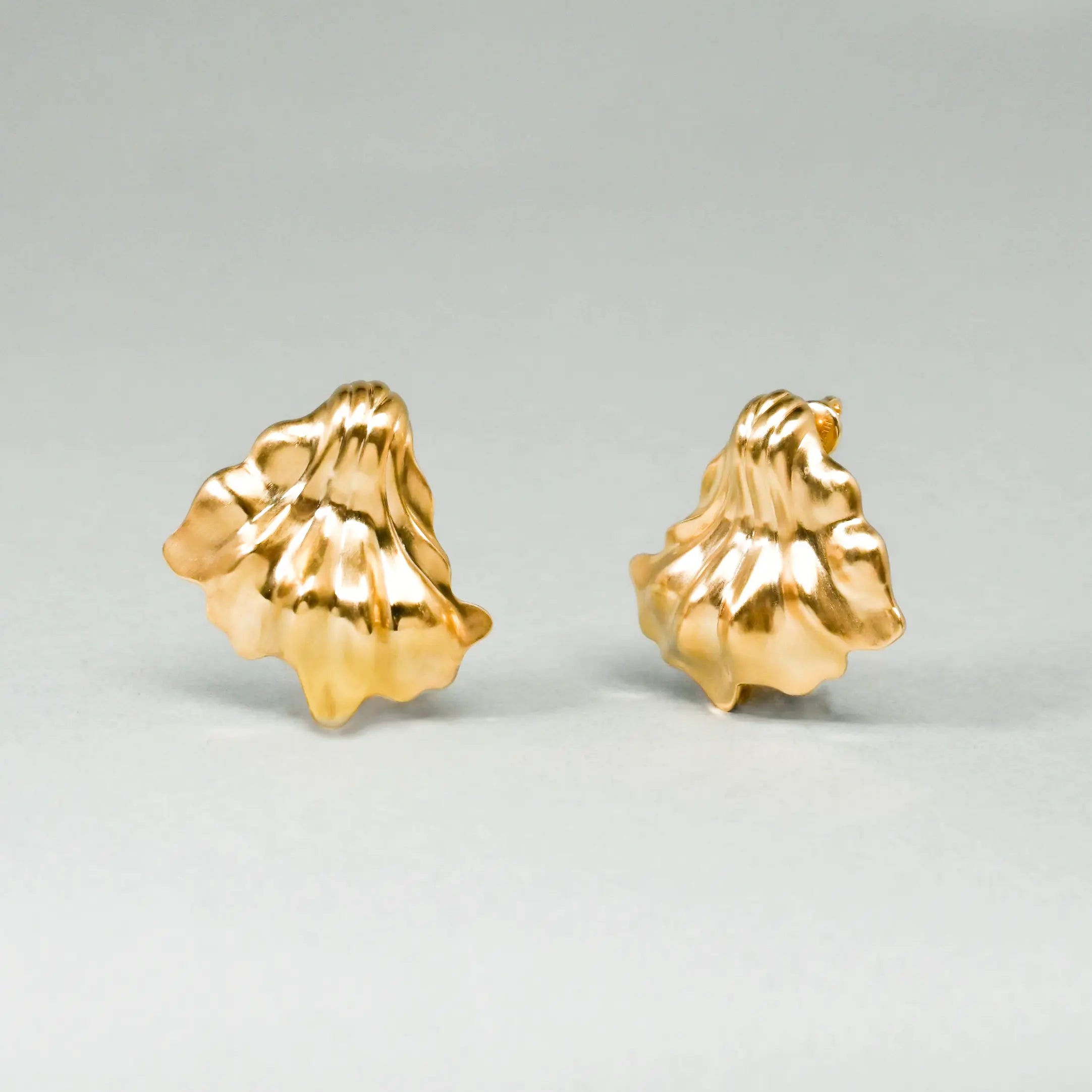 Pair of gold shell-shaped earrings on a light gray background