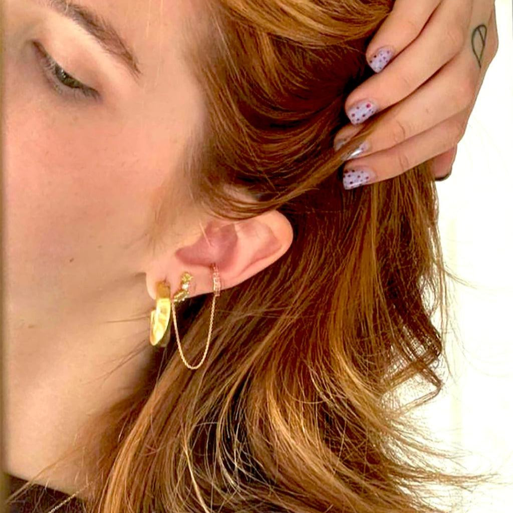 Peridot cluster studs layered with multiple gold earrings and chain cuff for trendy stacked look.