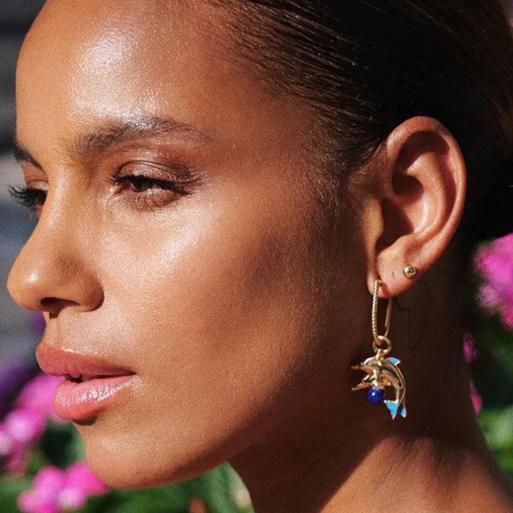 Gold dolphin charm earring with lapis lazuli bead, worn outdoors by model in natural light.