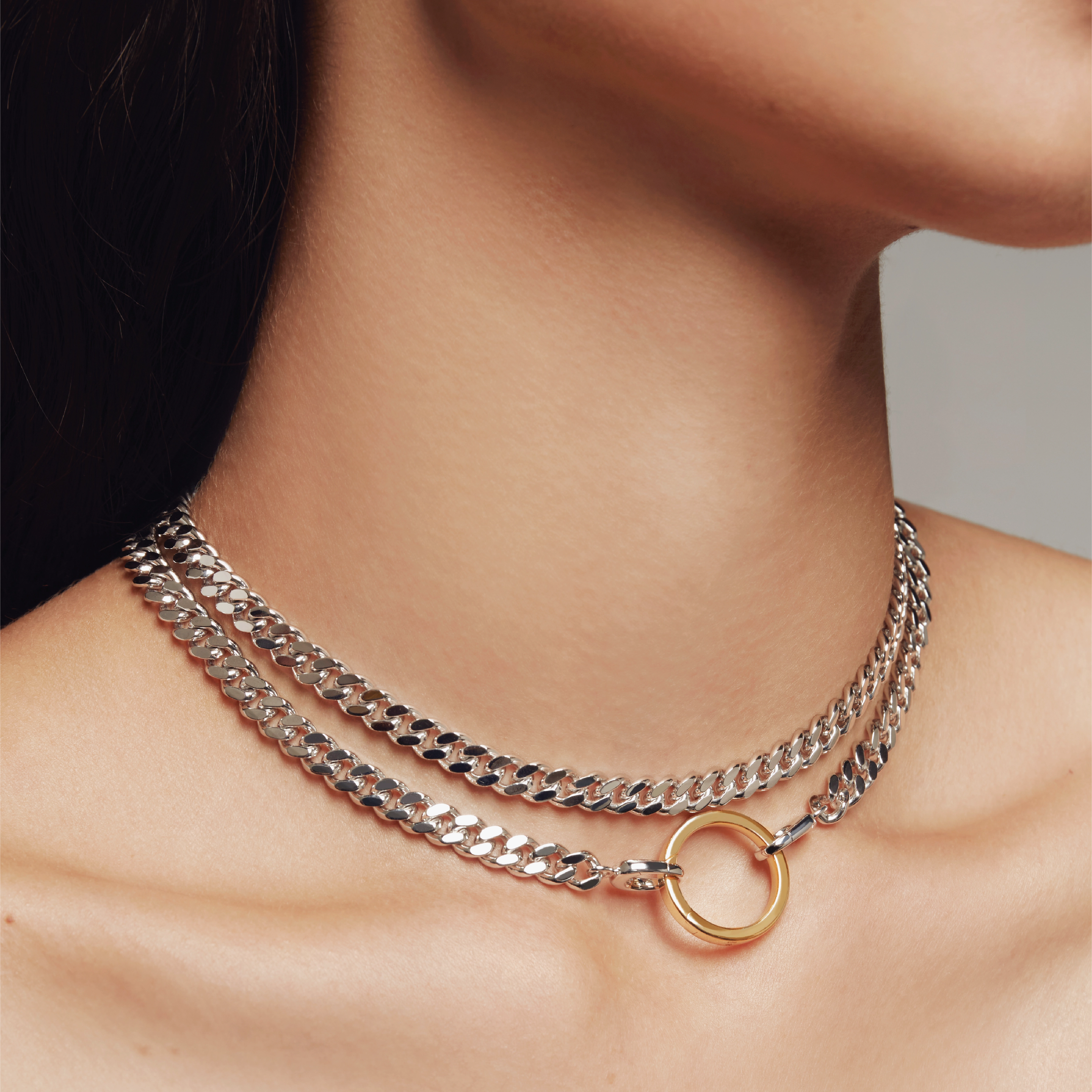 Close-up of a model wearing a double-layered silver chain choker with a gold circular pendant.