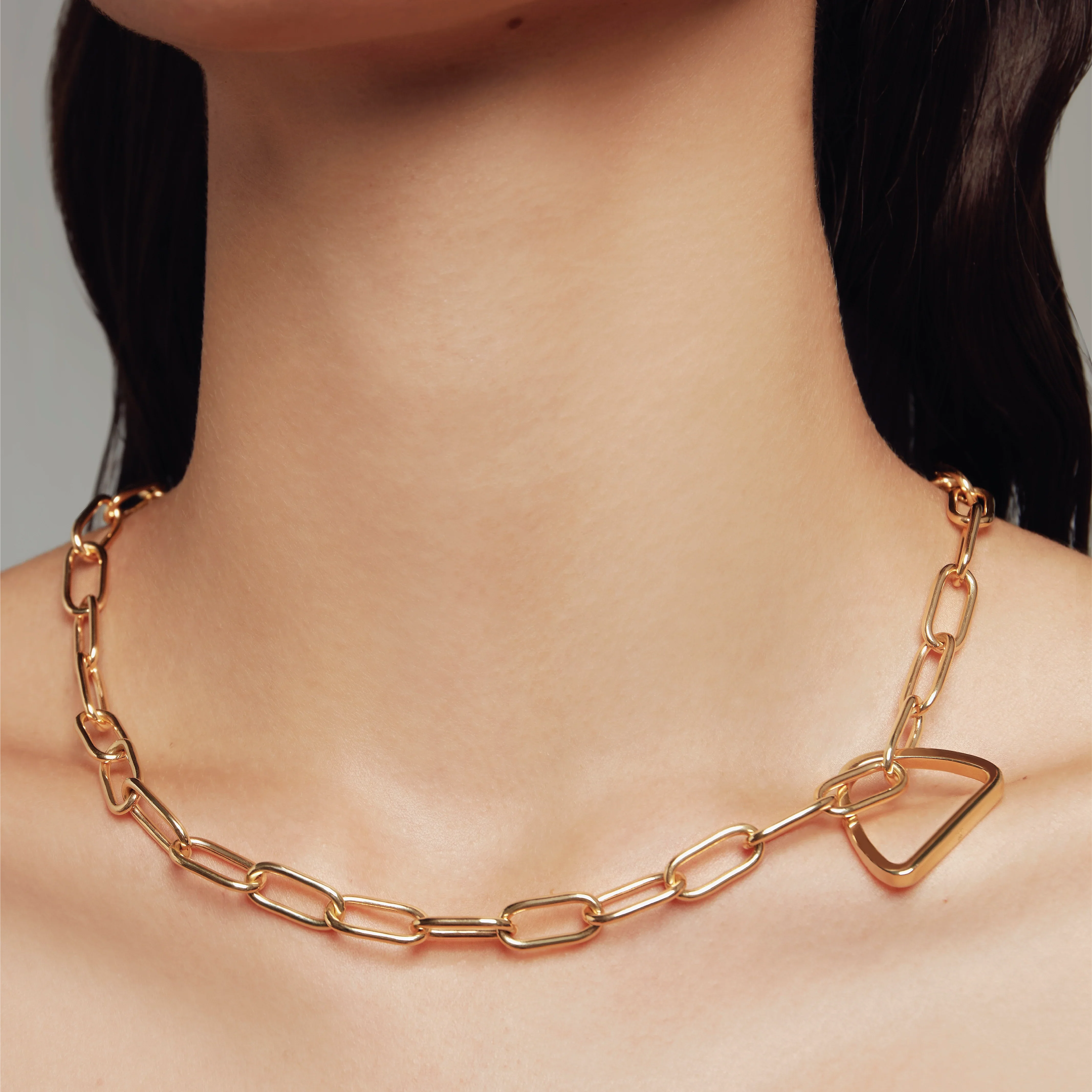 Close-up of a model wearing a gold paperclip chain necklace with a geometric triangle connector.