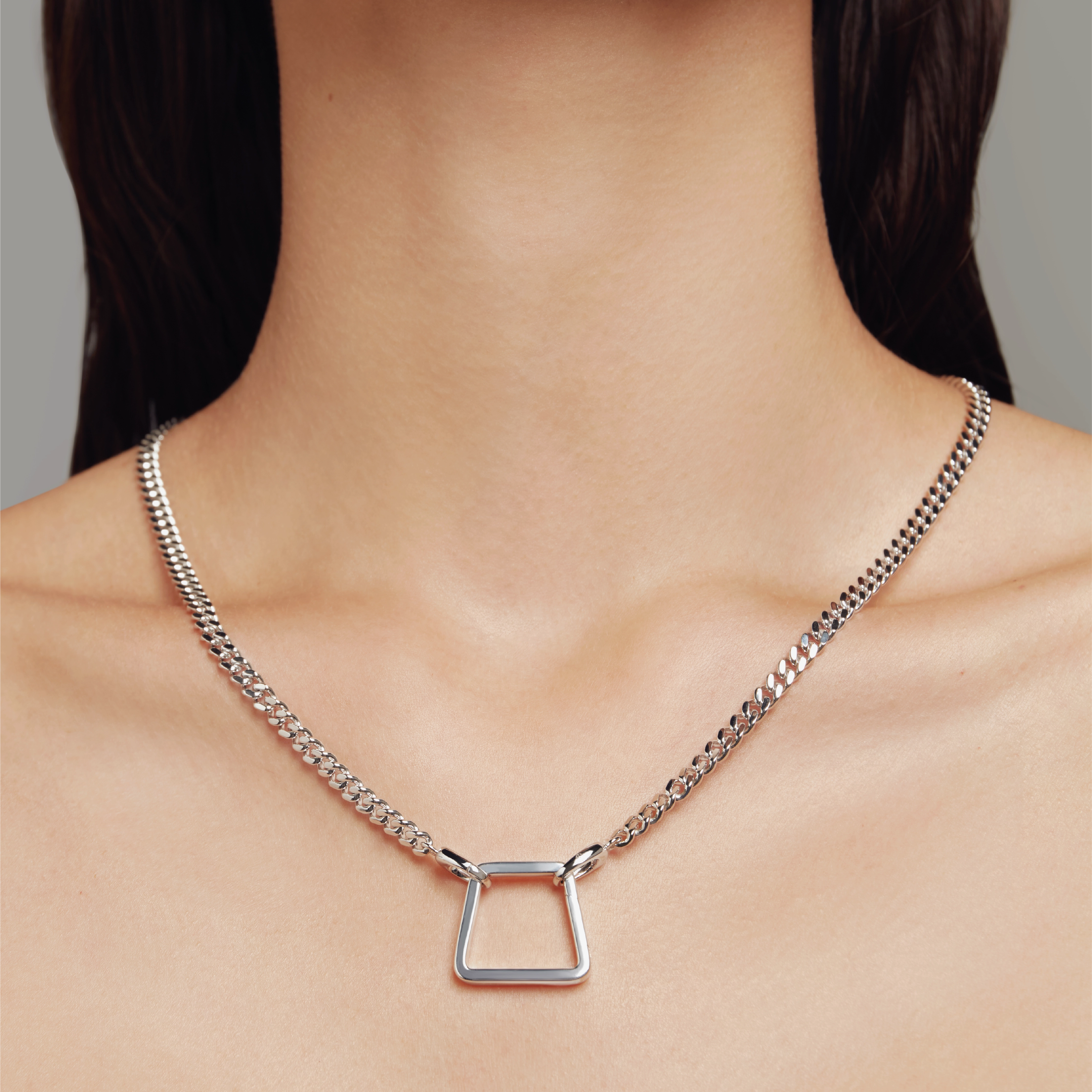 Close-up of a model wearing a silver chain necklace with a geometric trapezoid-shaped pendant.