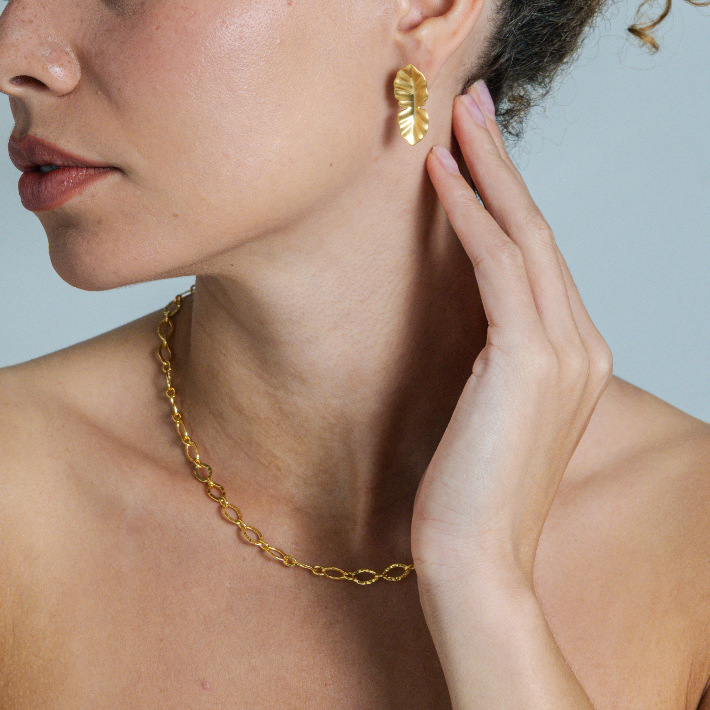 Close-up of a person wearing gold earrings and necklace against a light blue background