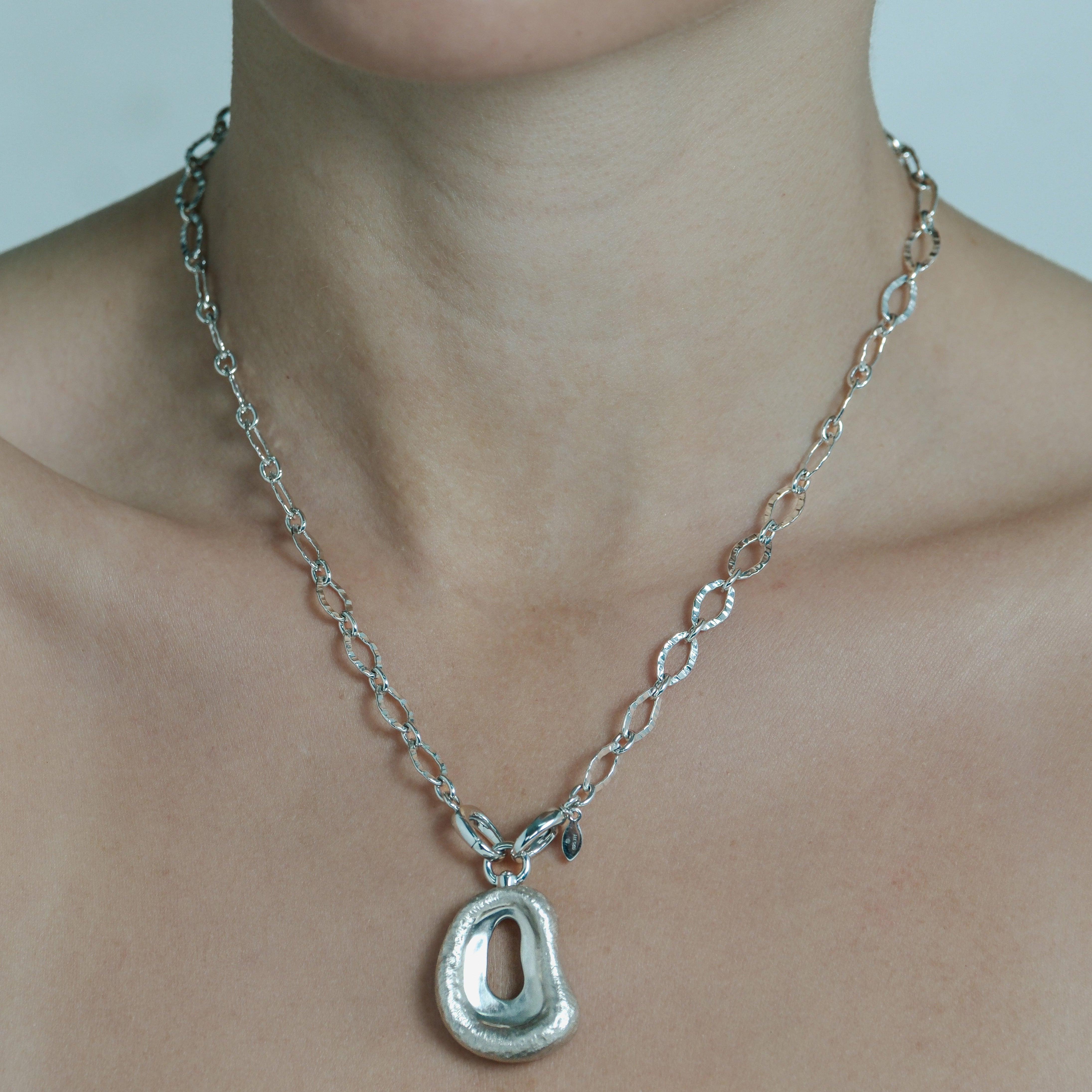 Silver necklace with a unique pendant on a person's neck against a neutral background