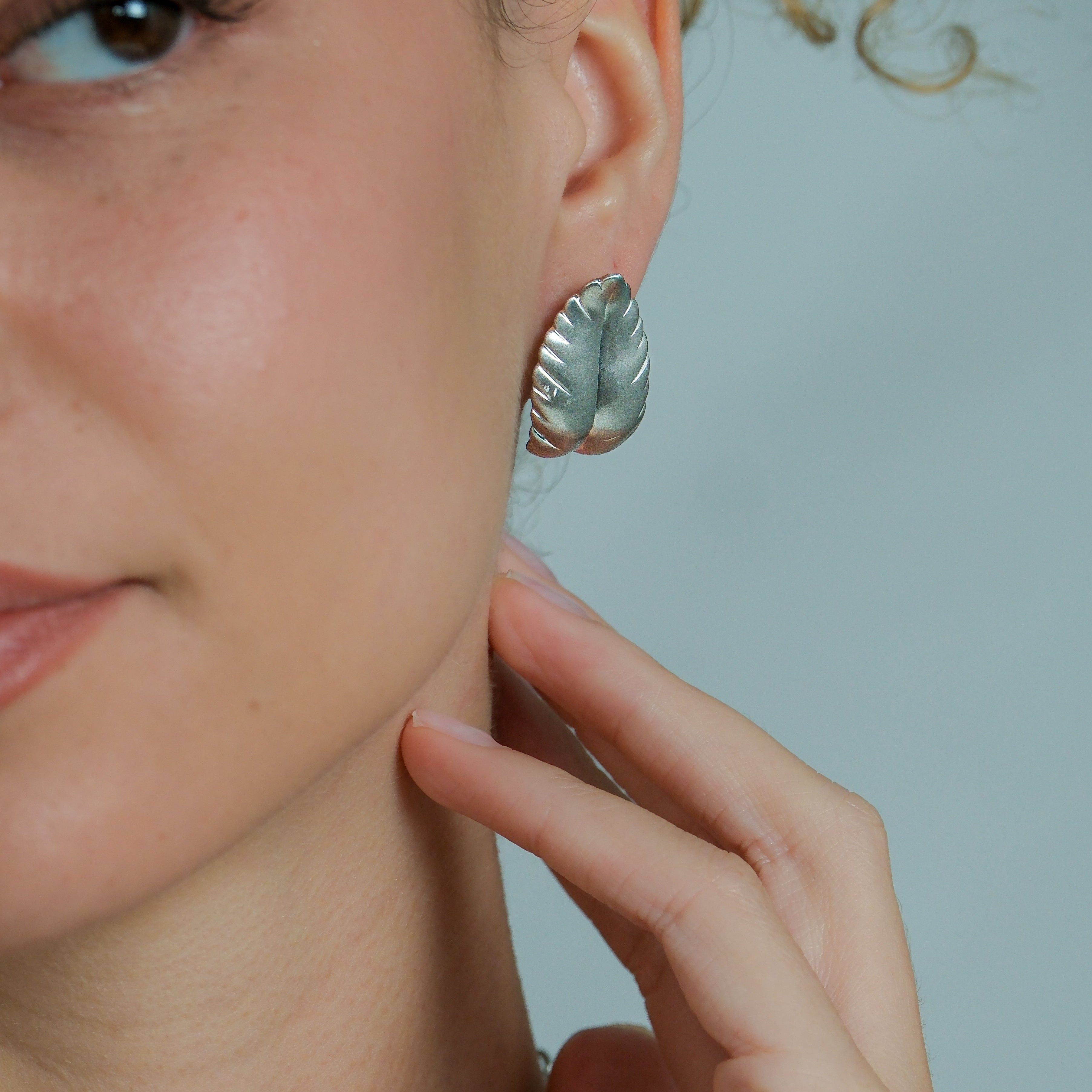 Close-up of a person wearing silver leaf-shaped earrings with a neutral background