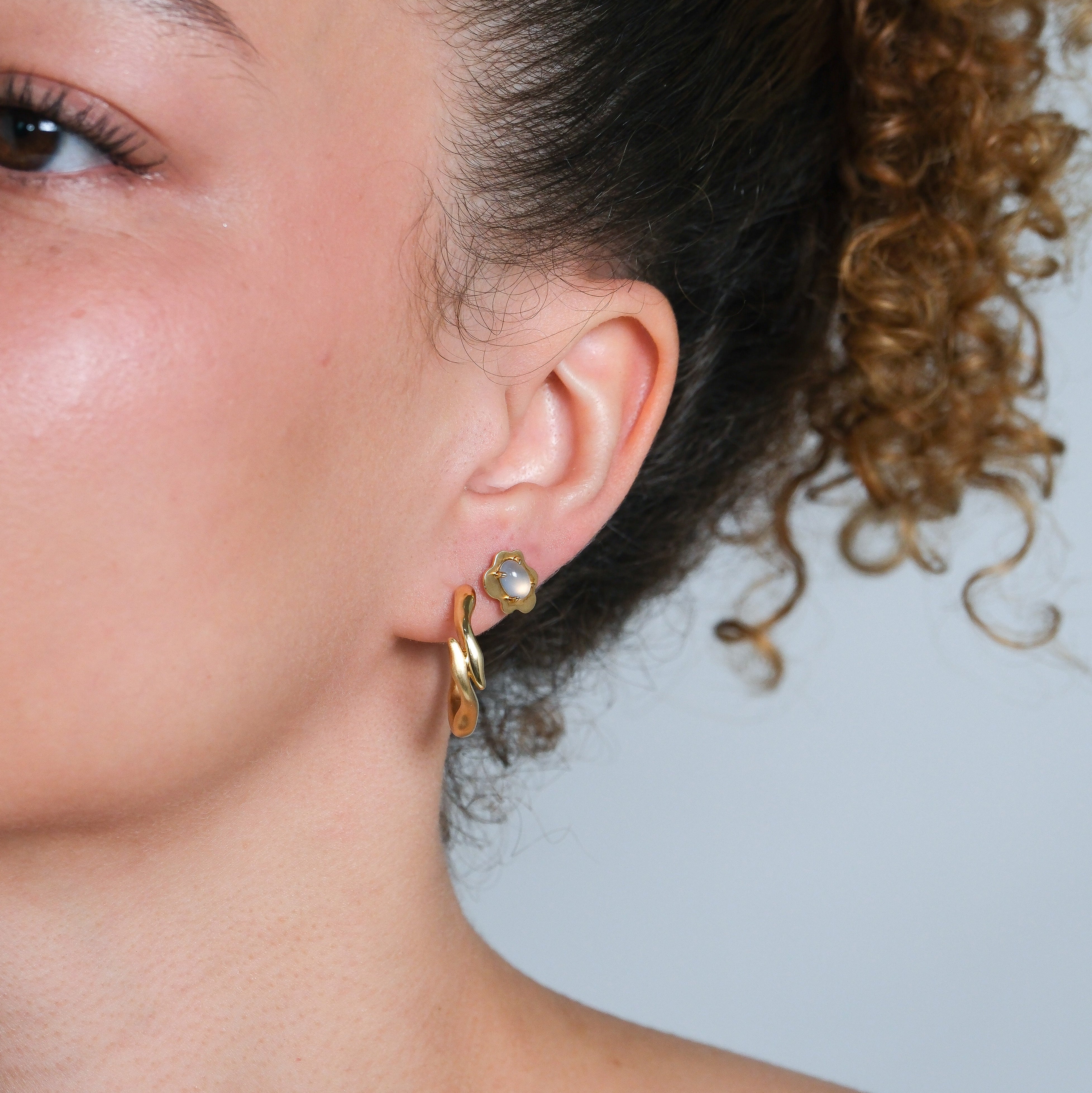 Close-up of a person wearing a gold earring with a gemstone on a neutral background