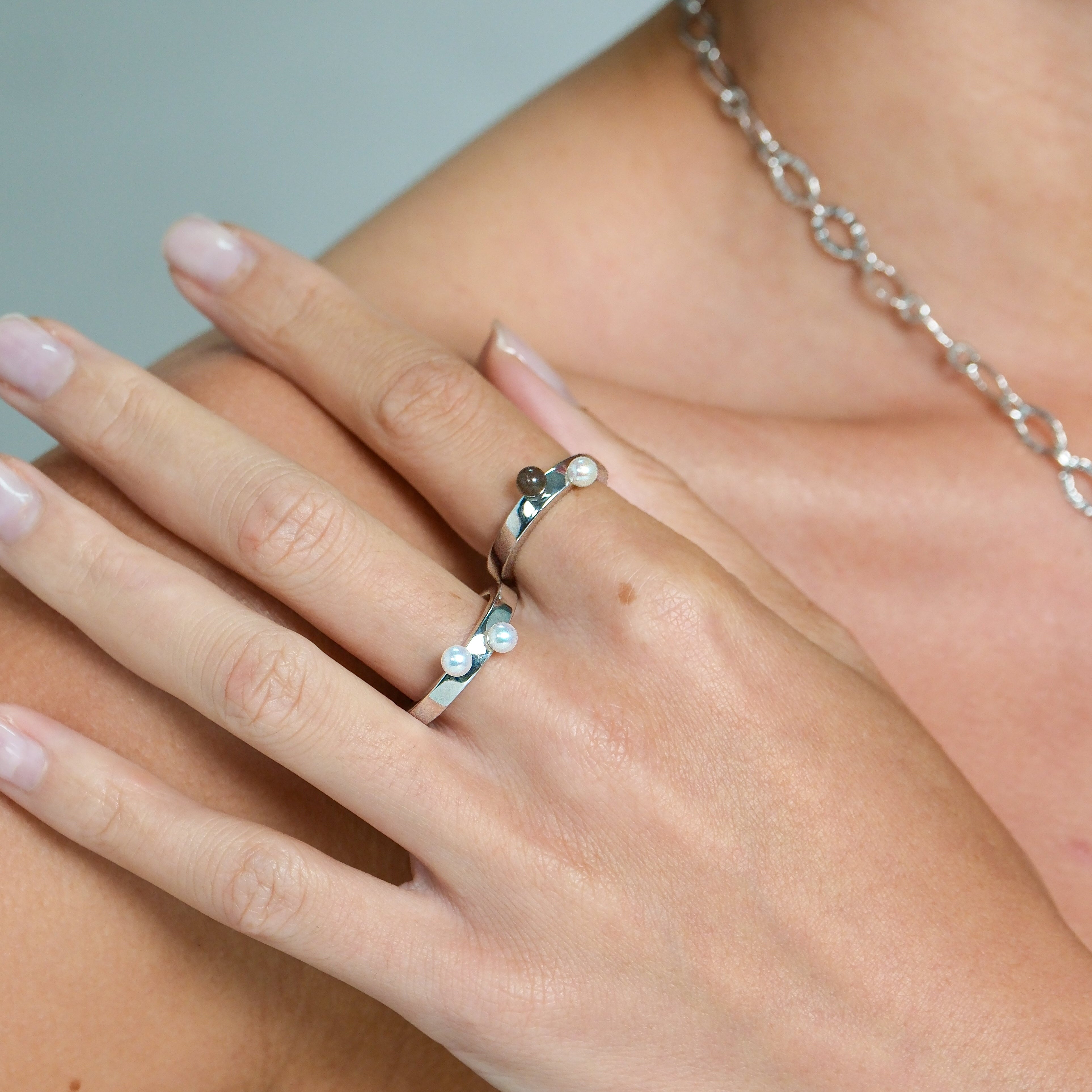 Close-up of a hand wearing a silver ring with a small gemstone, against a neutral background.