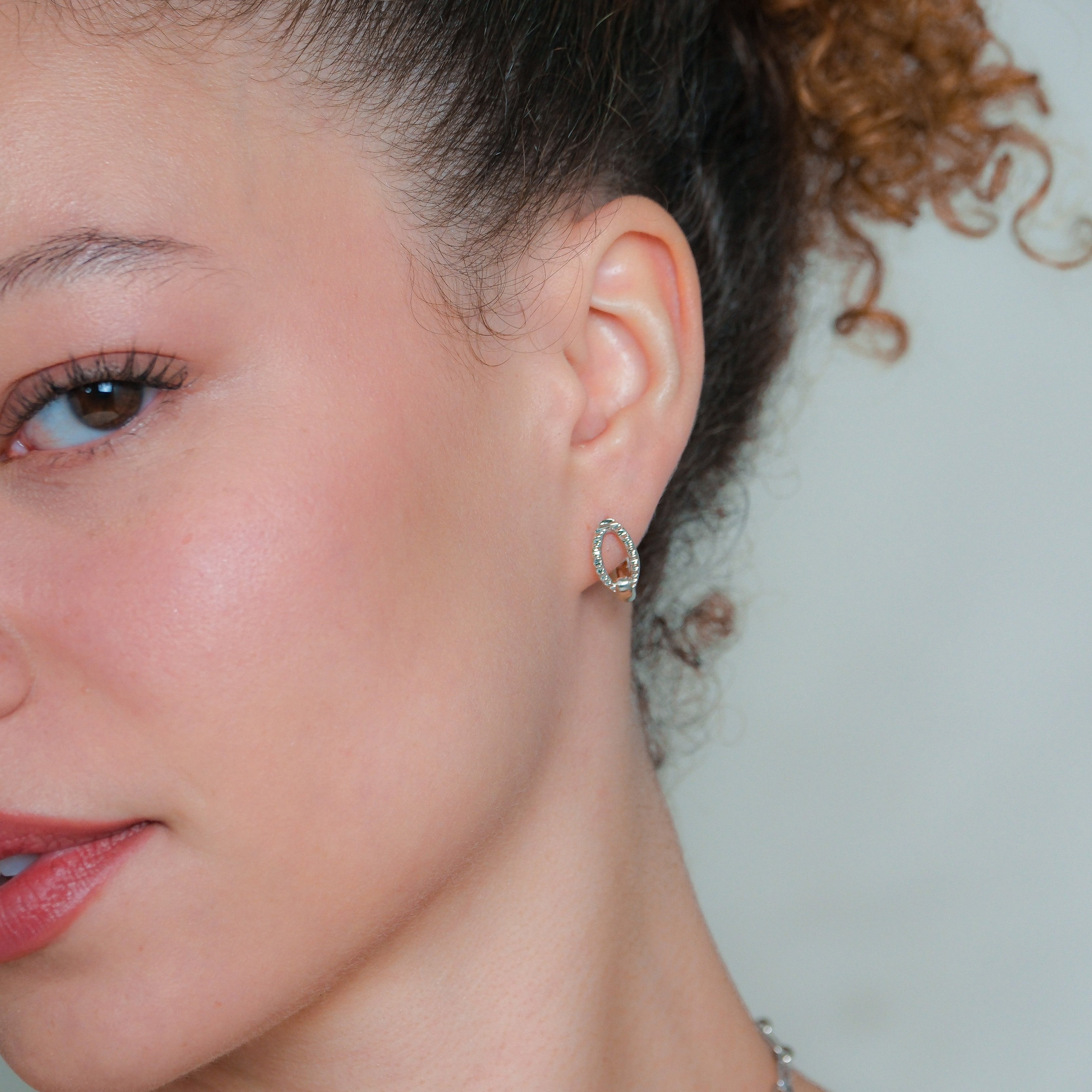 Close-up of a woman wearing a silver earring against a neutral background