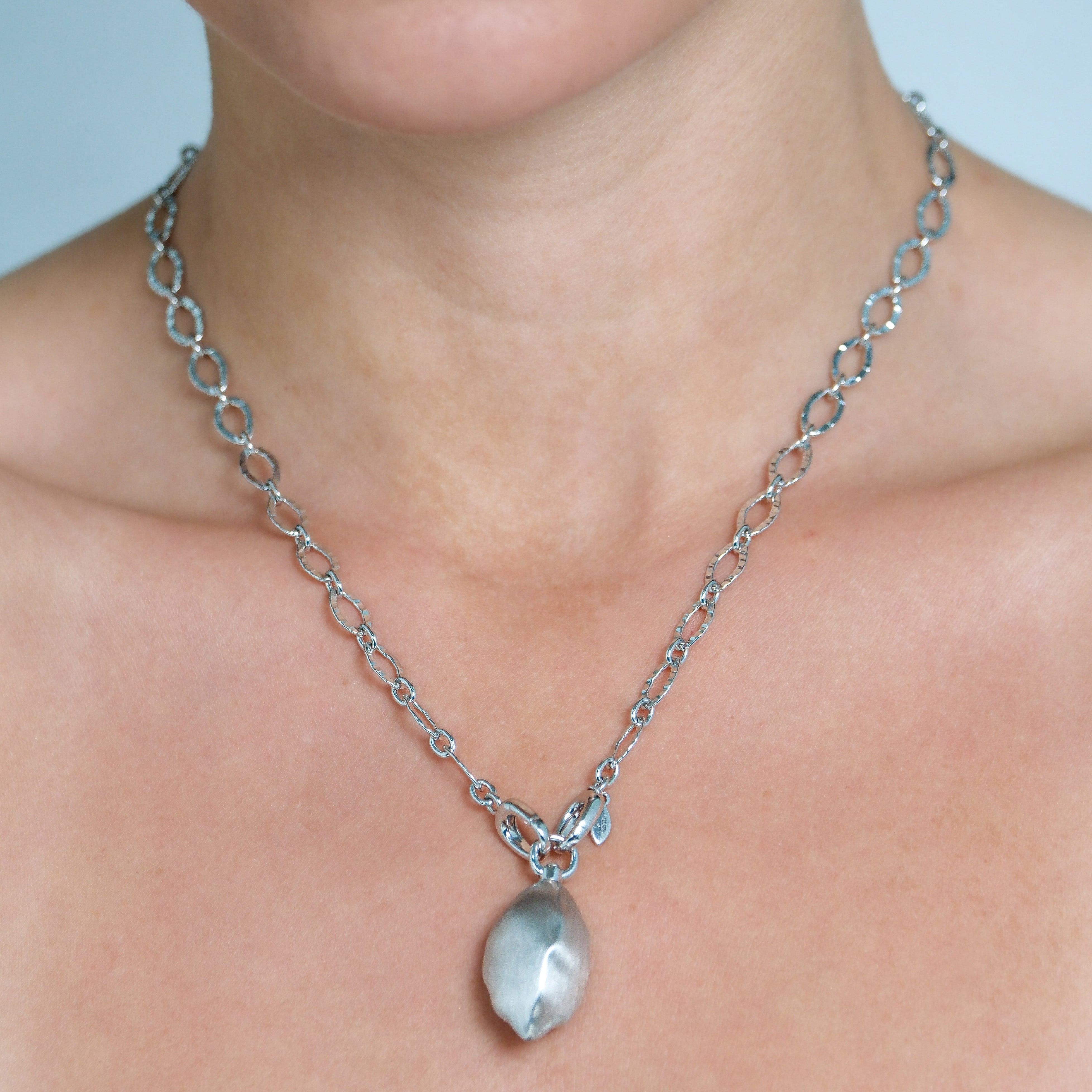Close-up of a silver chain necklace with a pendant on a person's neck.