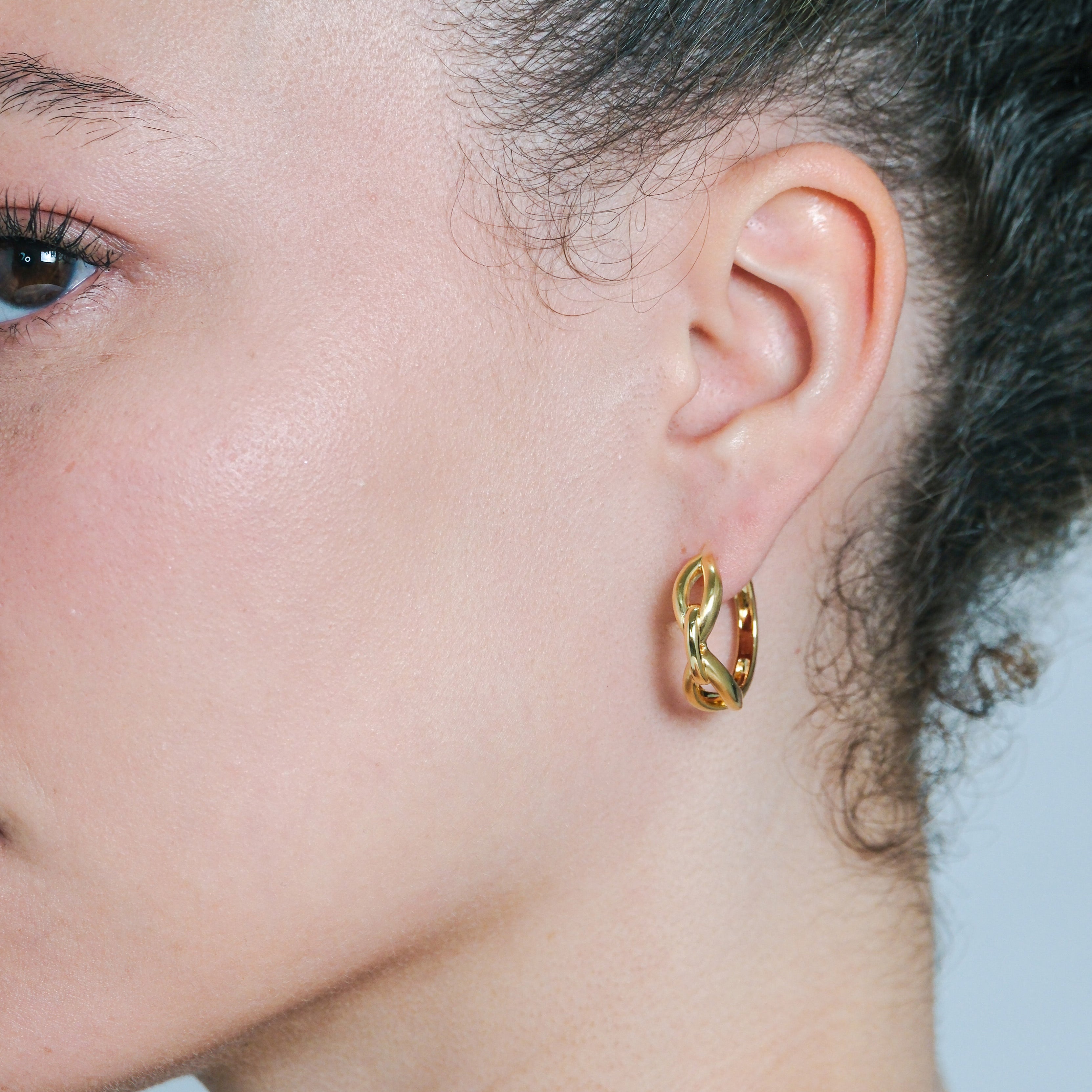 Close-up of a person wearing a gold hoop earring against a neutral background