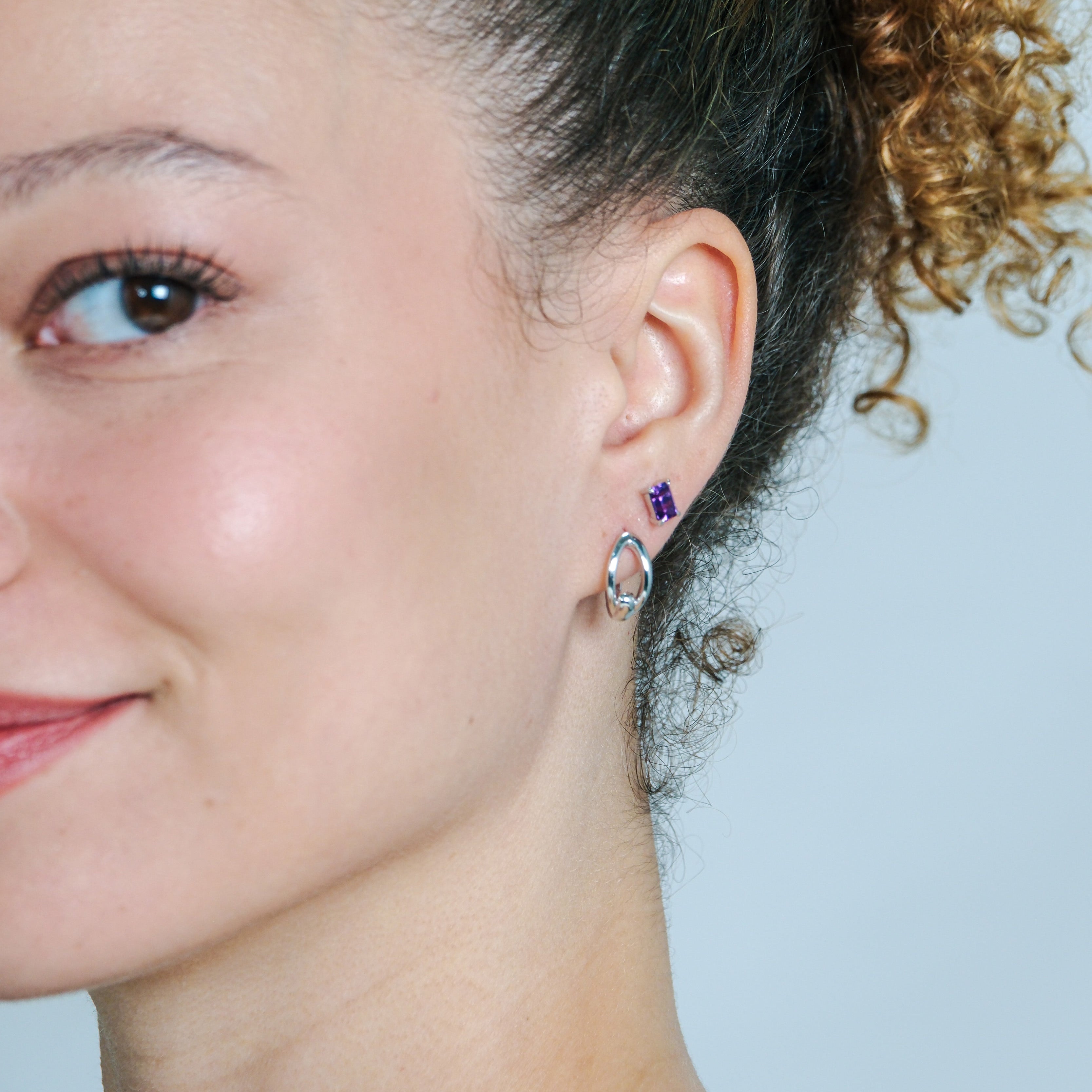 Close-up of a woman wearing a purple gemstone earring against a light blue background