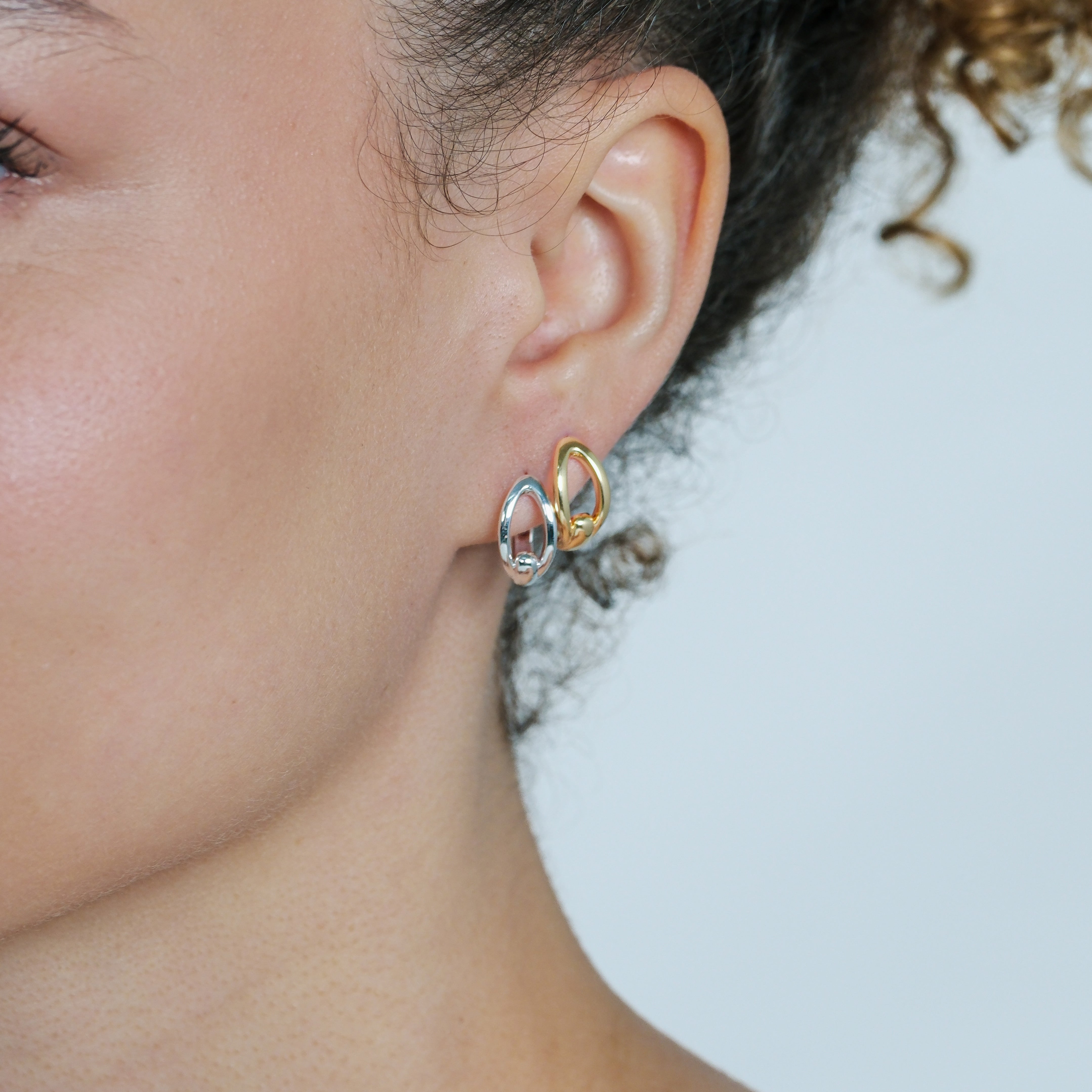 Close-up of a person wearing gold and silver hoop earrings with a light background