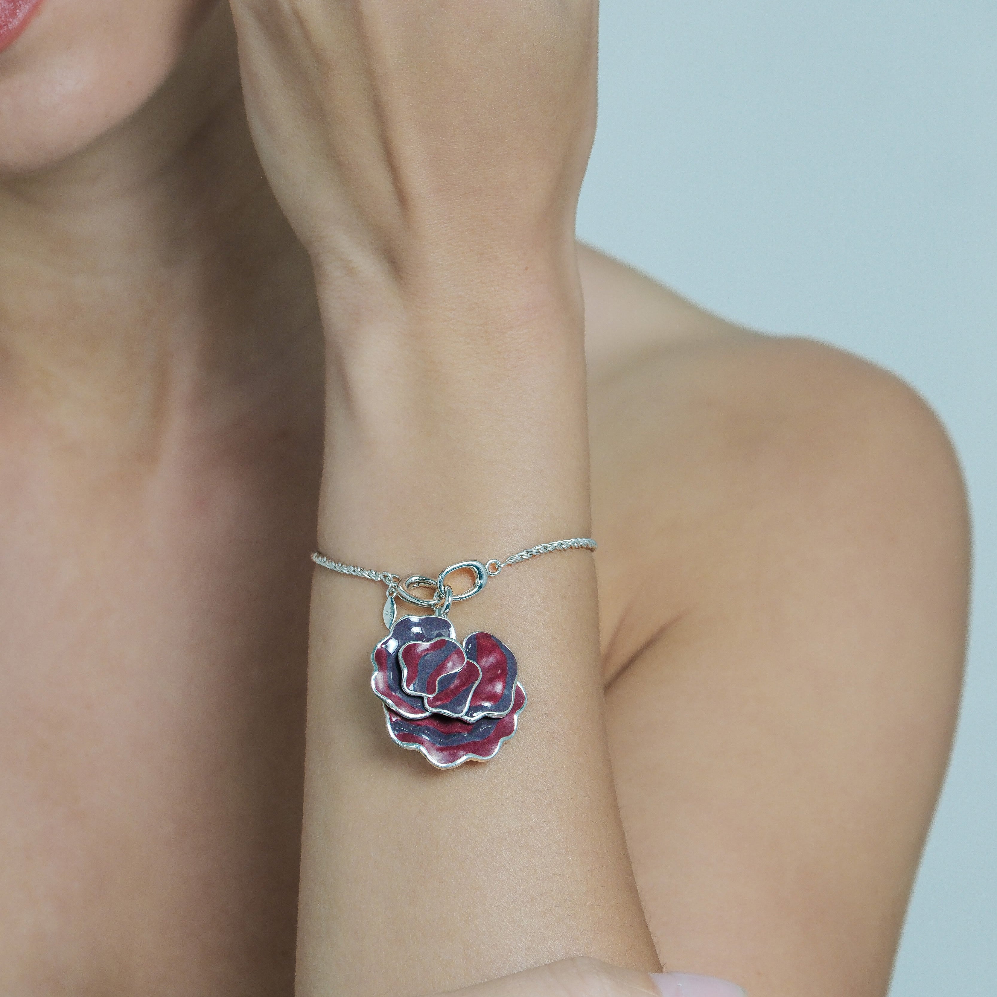 Close-up of a person wearing a silver bracelet with a floral charm on a plain background