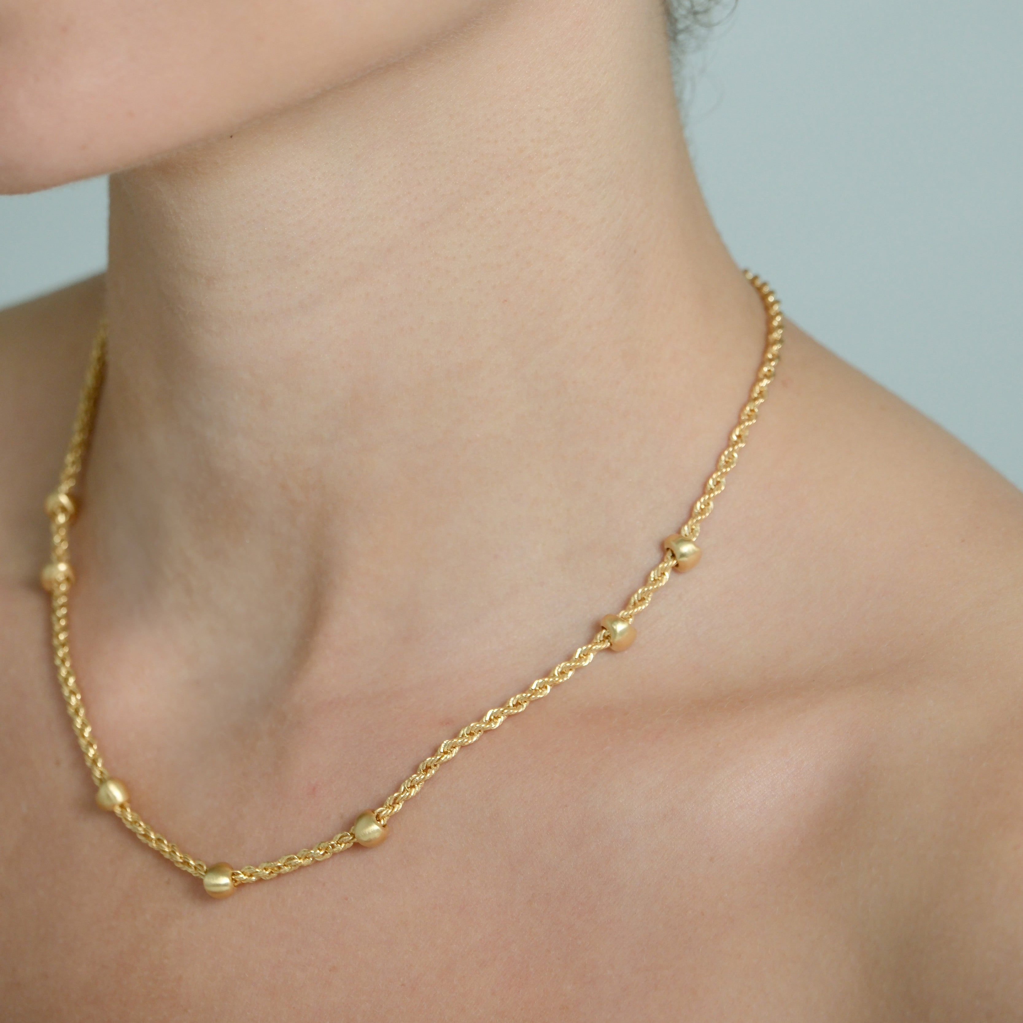 Close-up of a person wearing gold earrings and necklace against a neutral background