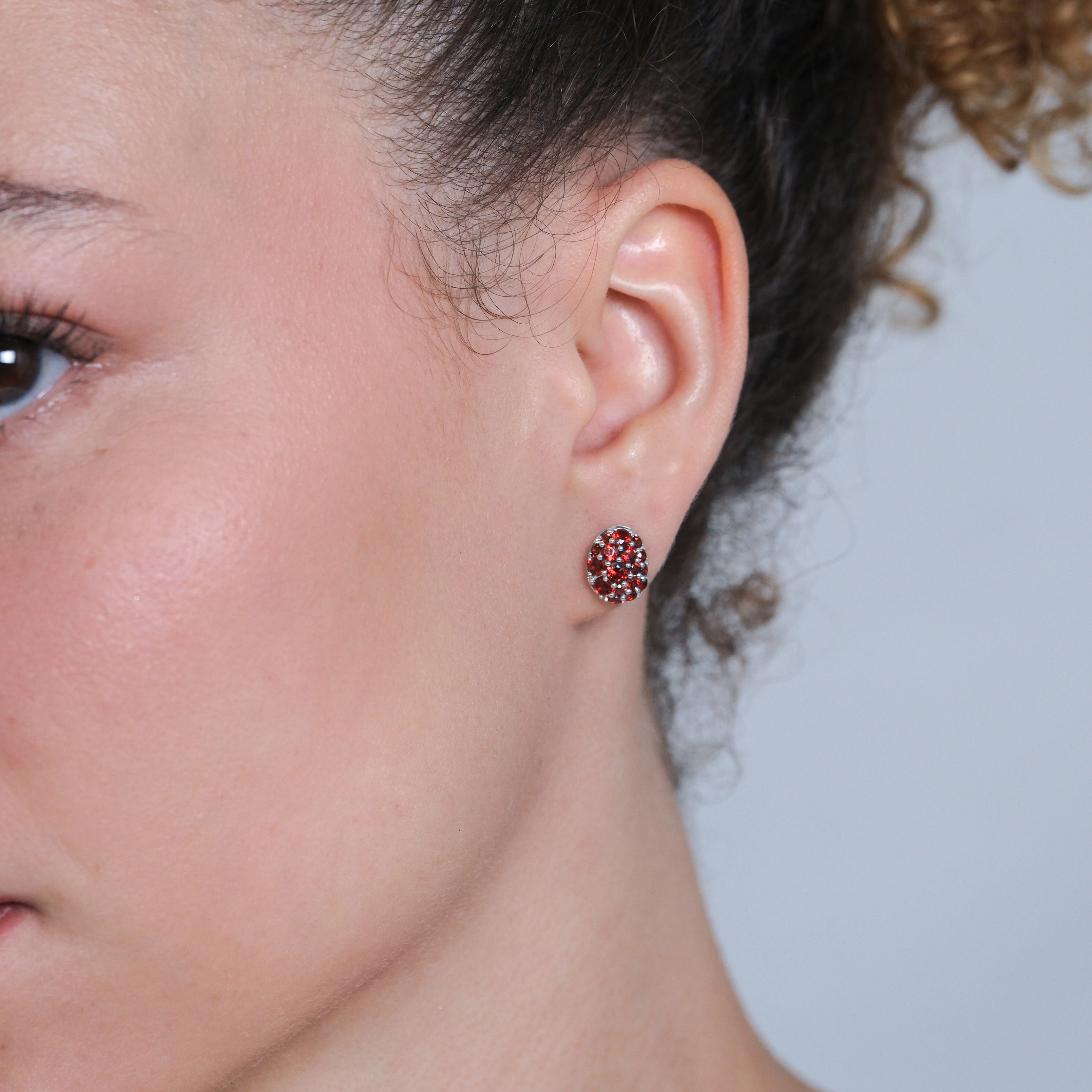 Close-up of a person wearing a stud earring with red stones on a light blue background