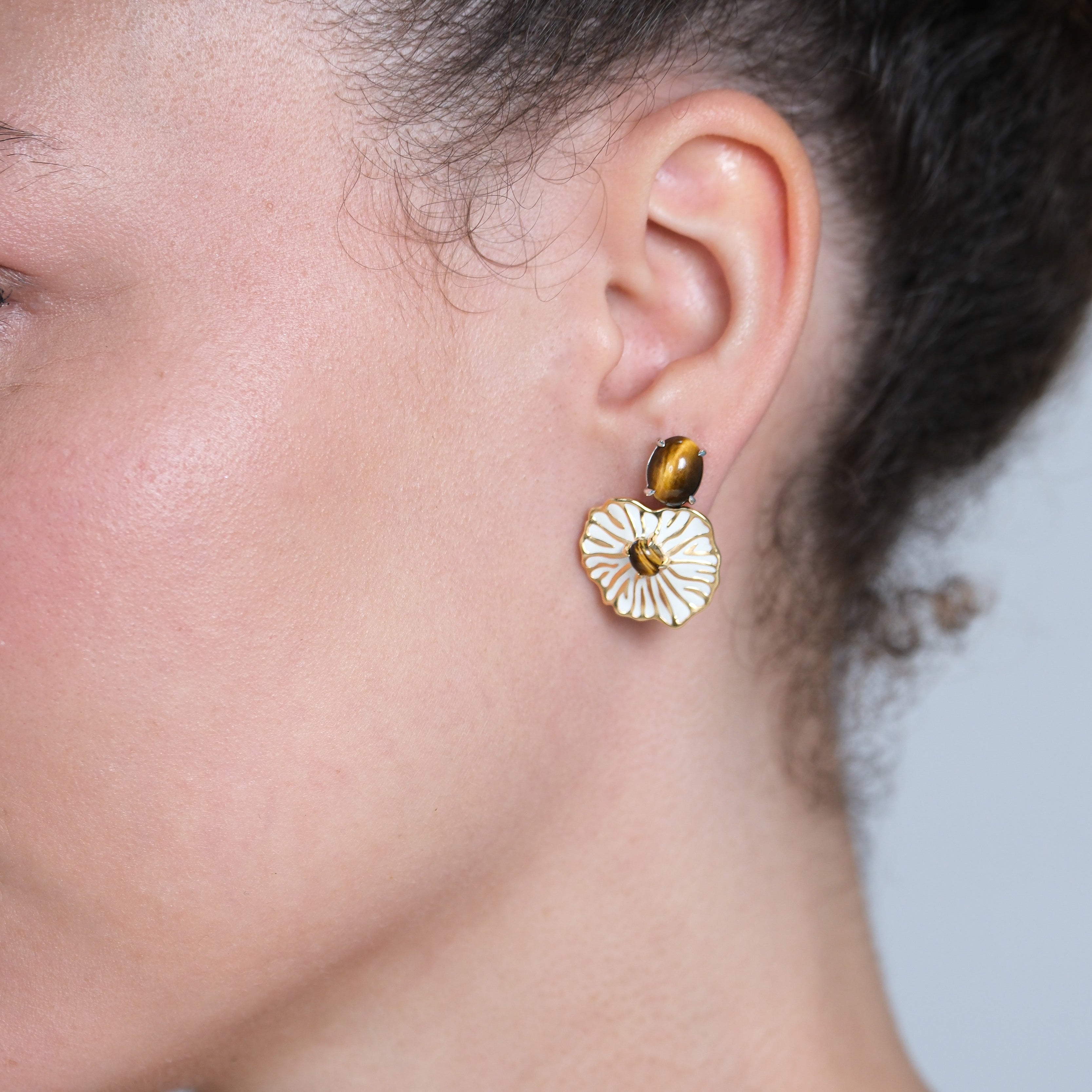 Close-up of a person wearing a brown stud and a gold earring with a floral design.