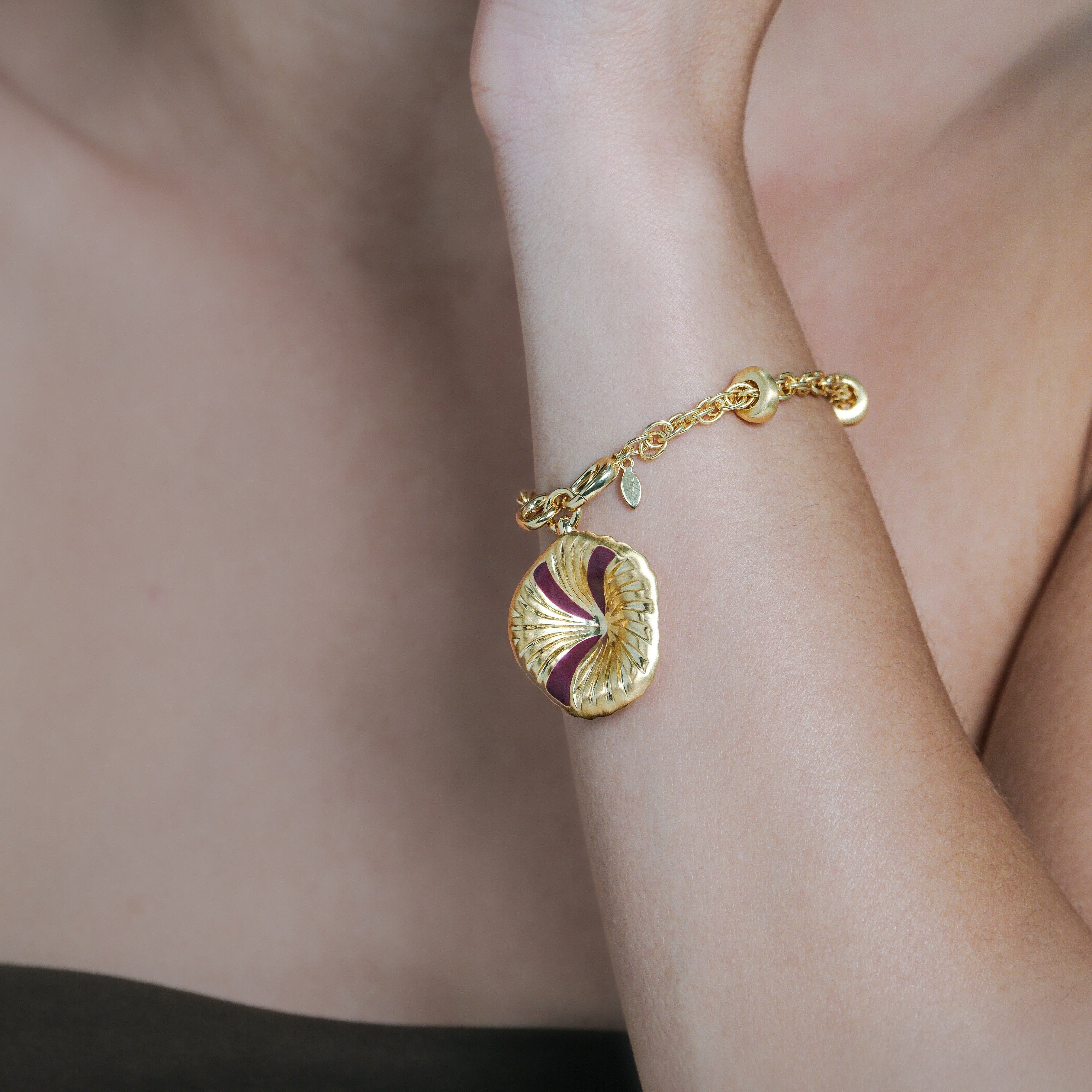 Gold bracelet with a gold charm on a person's wrist against a neutral background