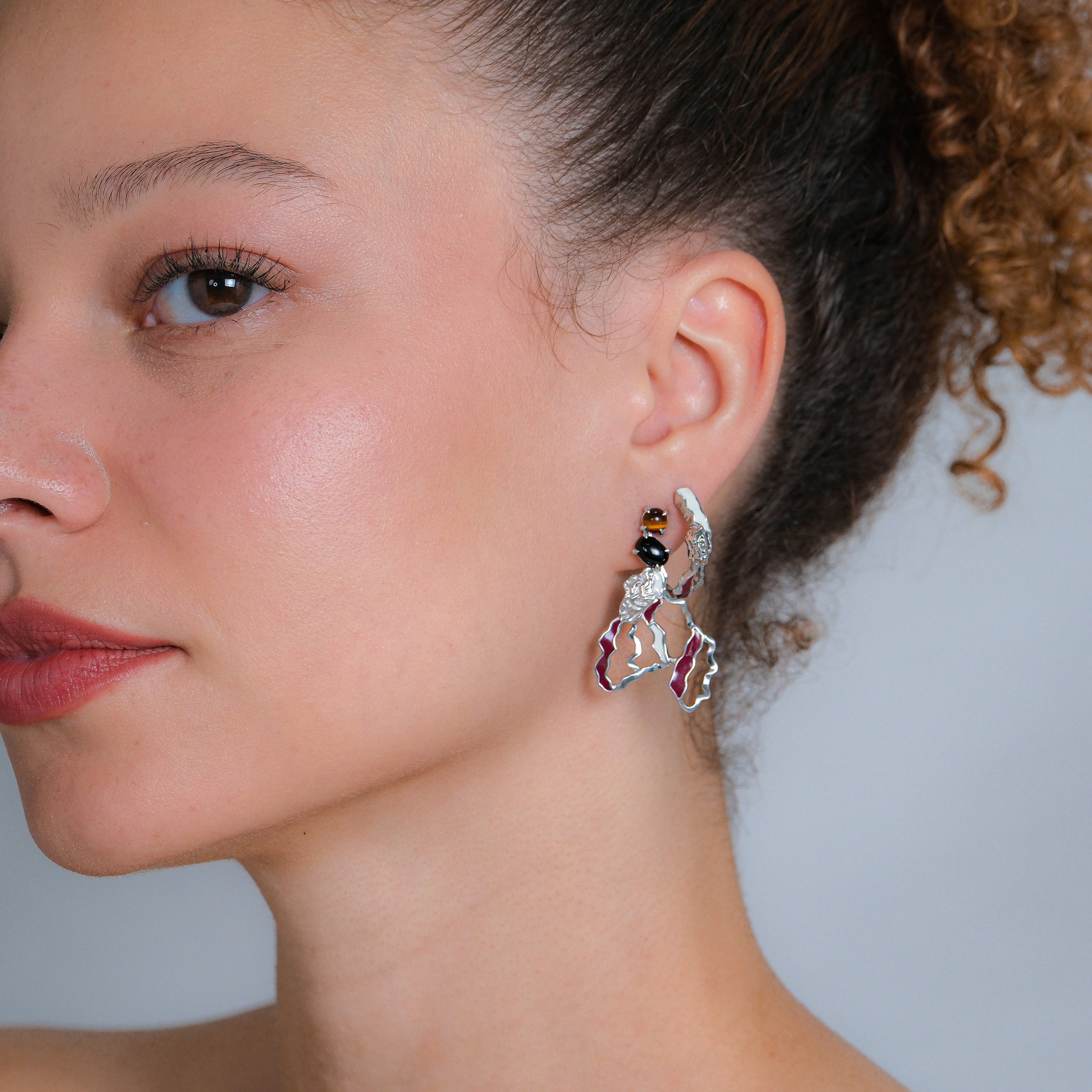 Close-up of a woman wearing a unique earring with a neutral background