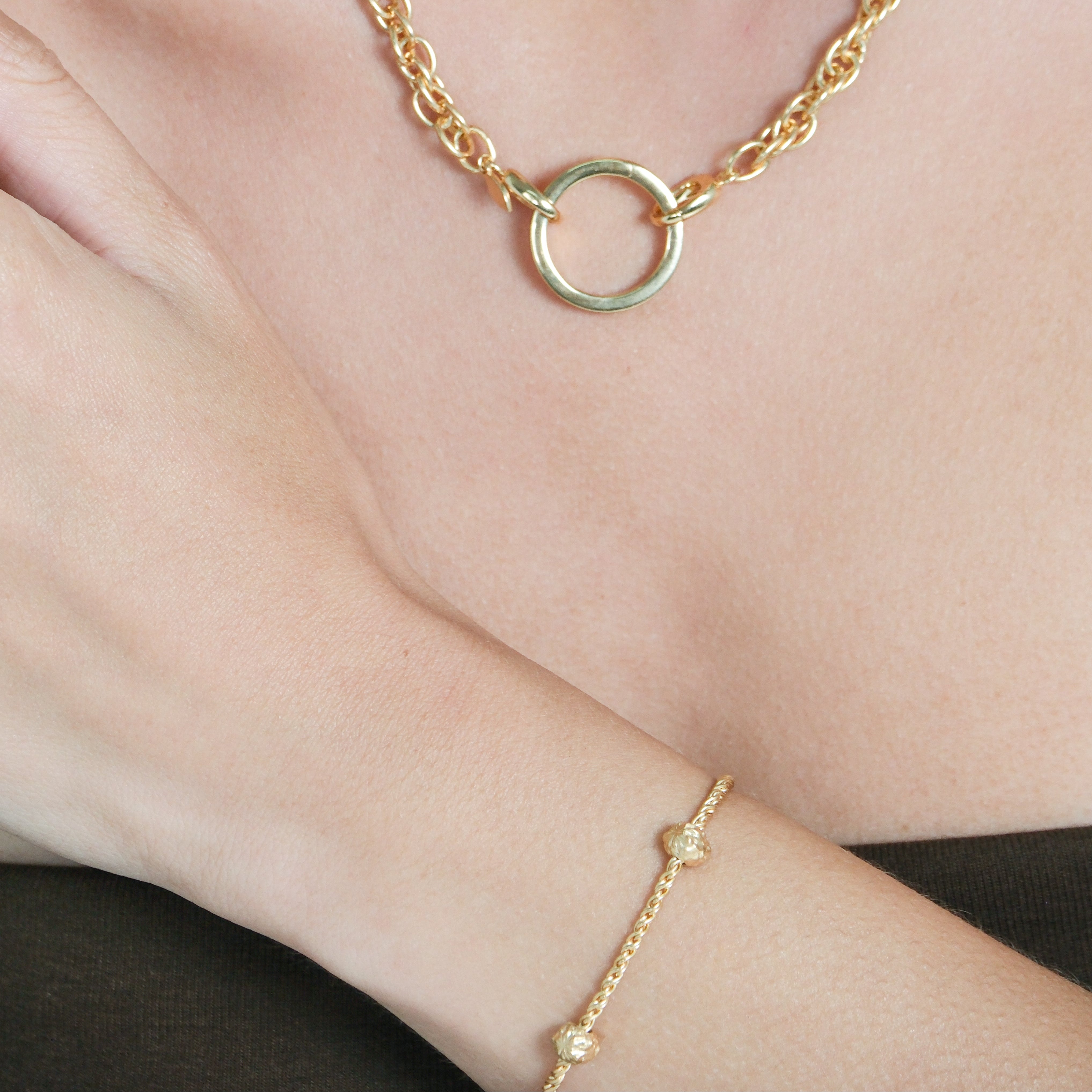 Gold bracelet with a circular clasp on a wrist against a neutral background