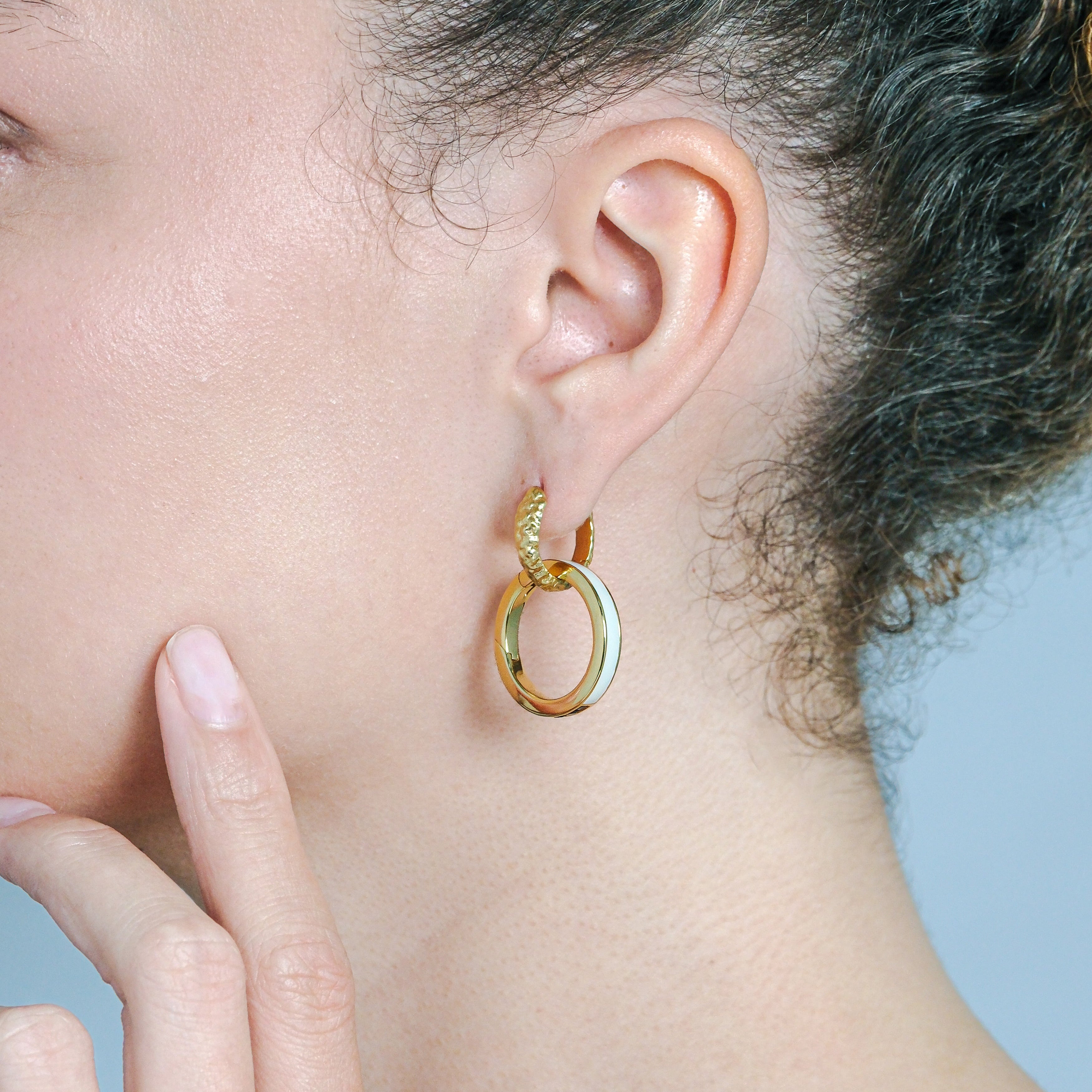 Close-up of a person wearing gold hoop earrings with a neutral background