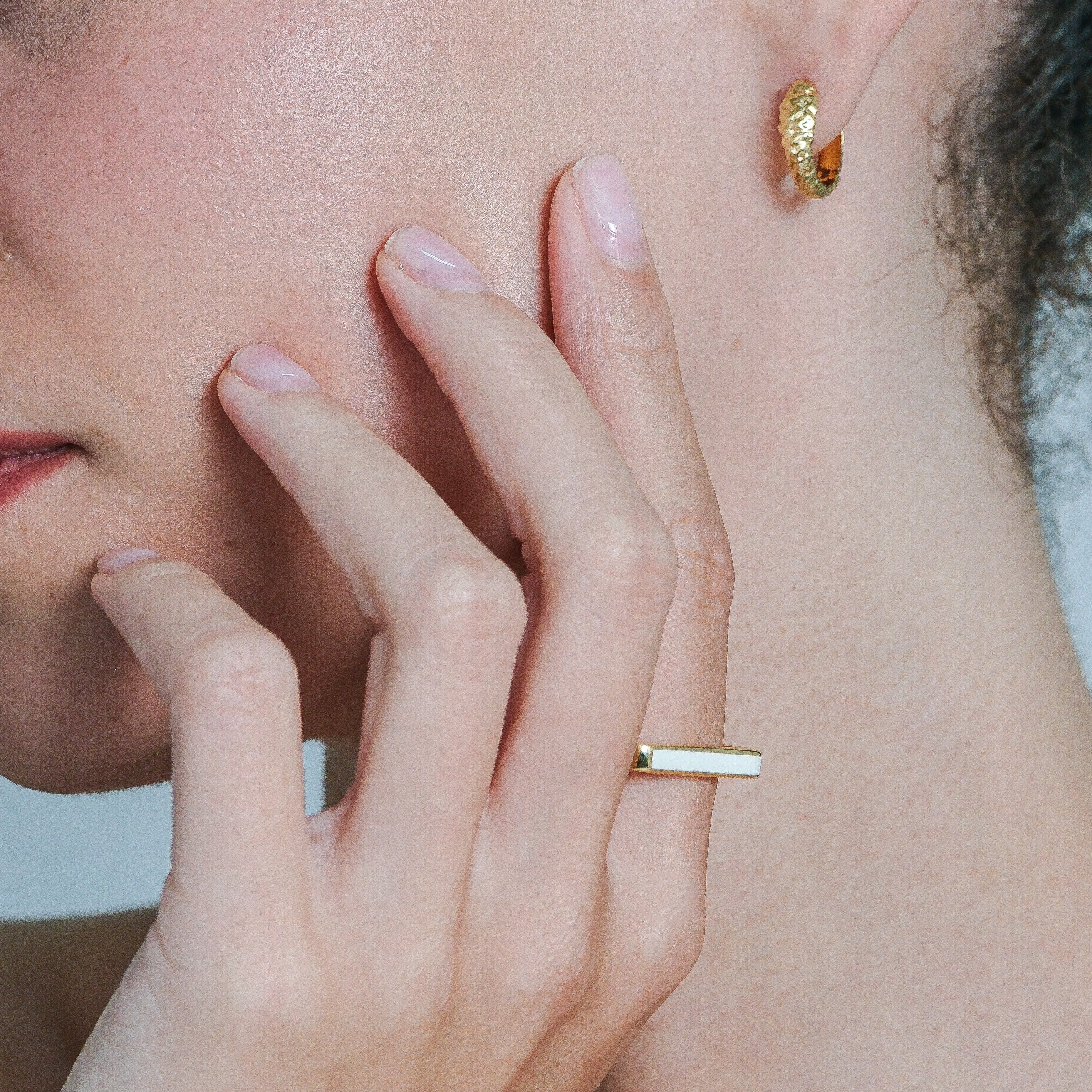 Close-up of a person wearing gold hoop earrings and a gold ring.