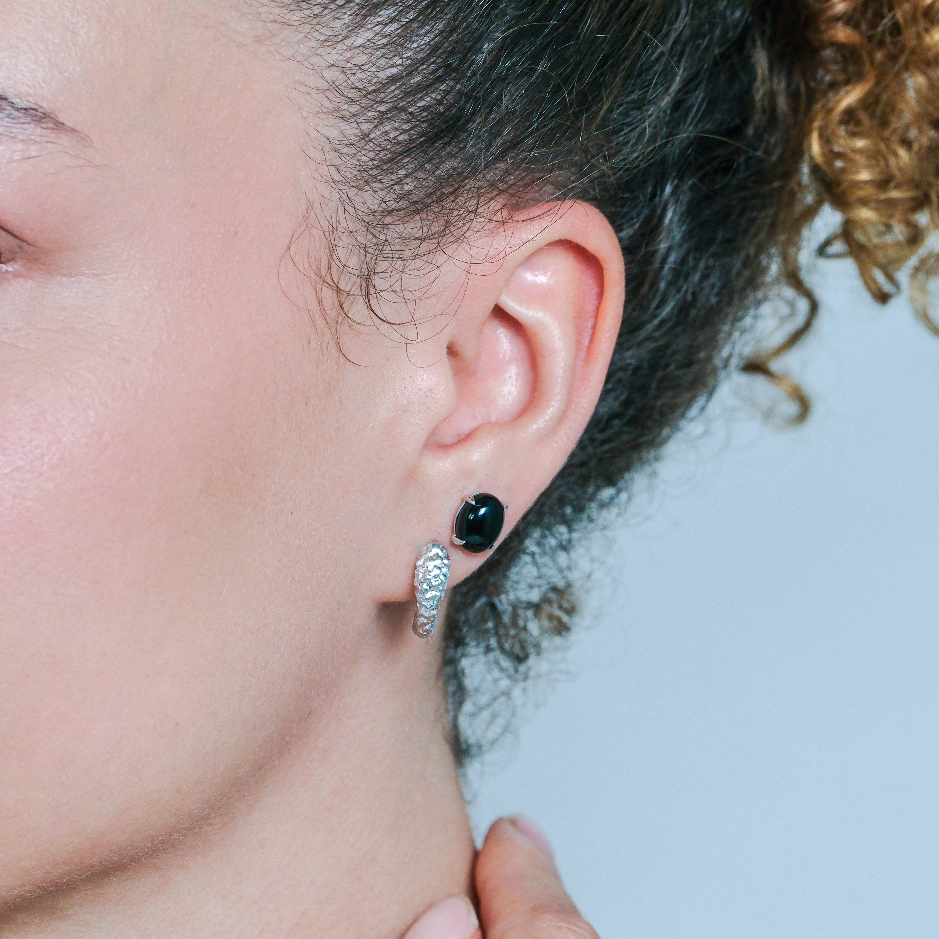 Close-up of a person wearing a black earring with a silver hoop.