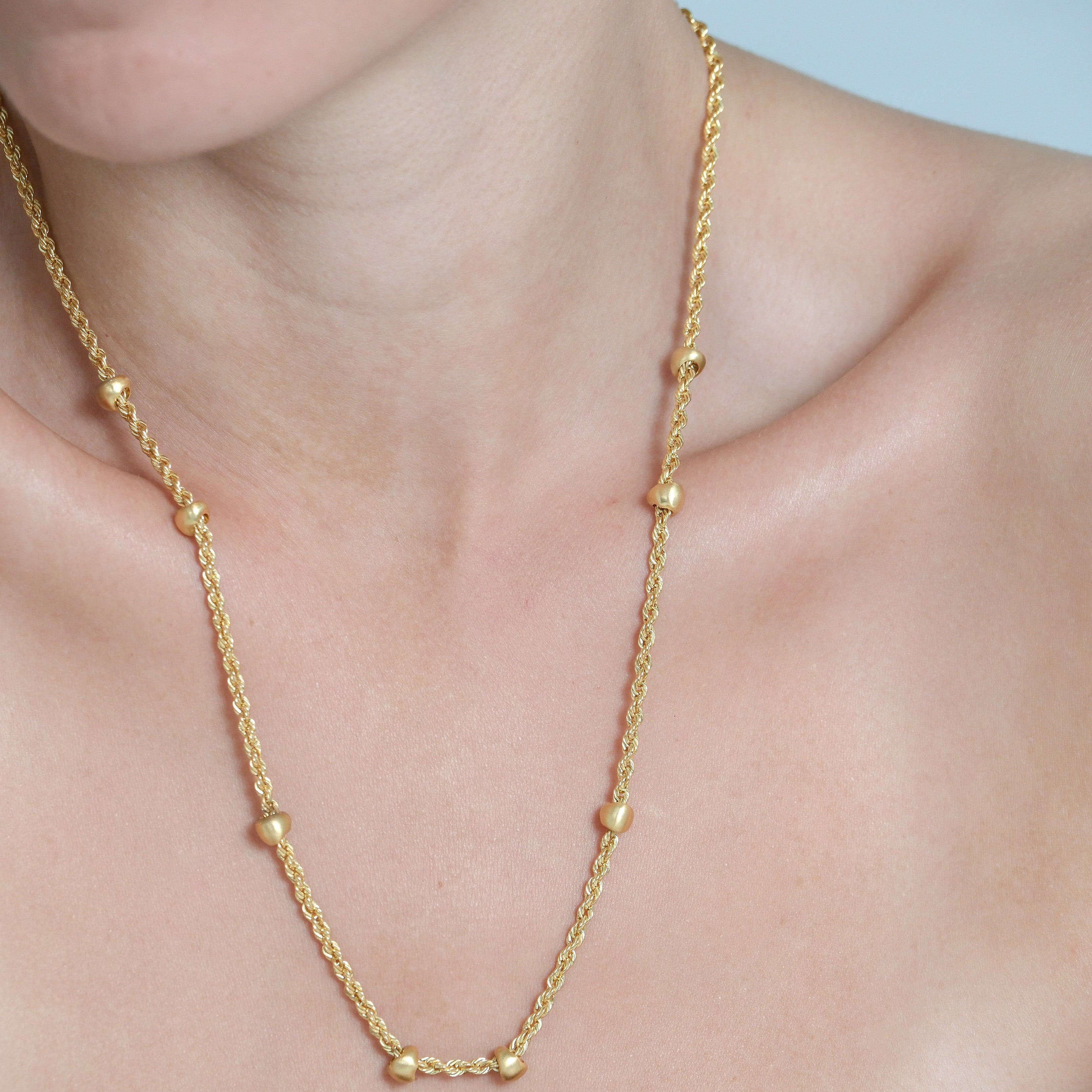 Gold necklace being worn on a person's neck with a plain background
