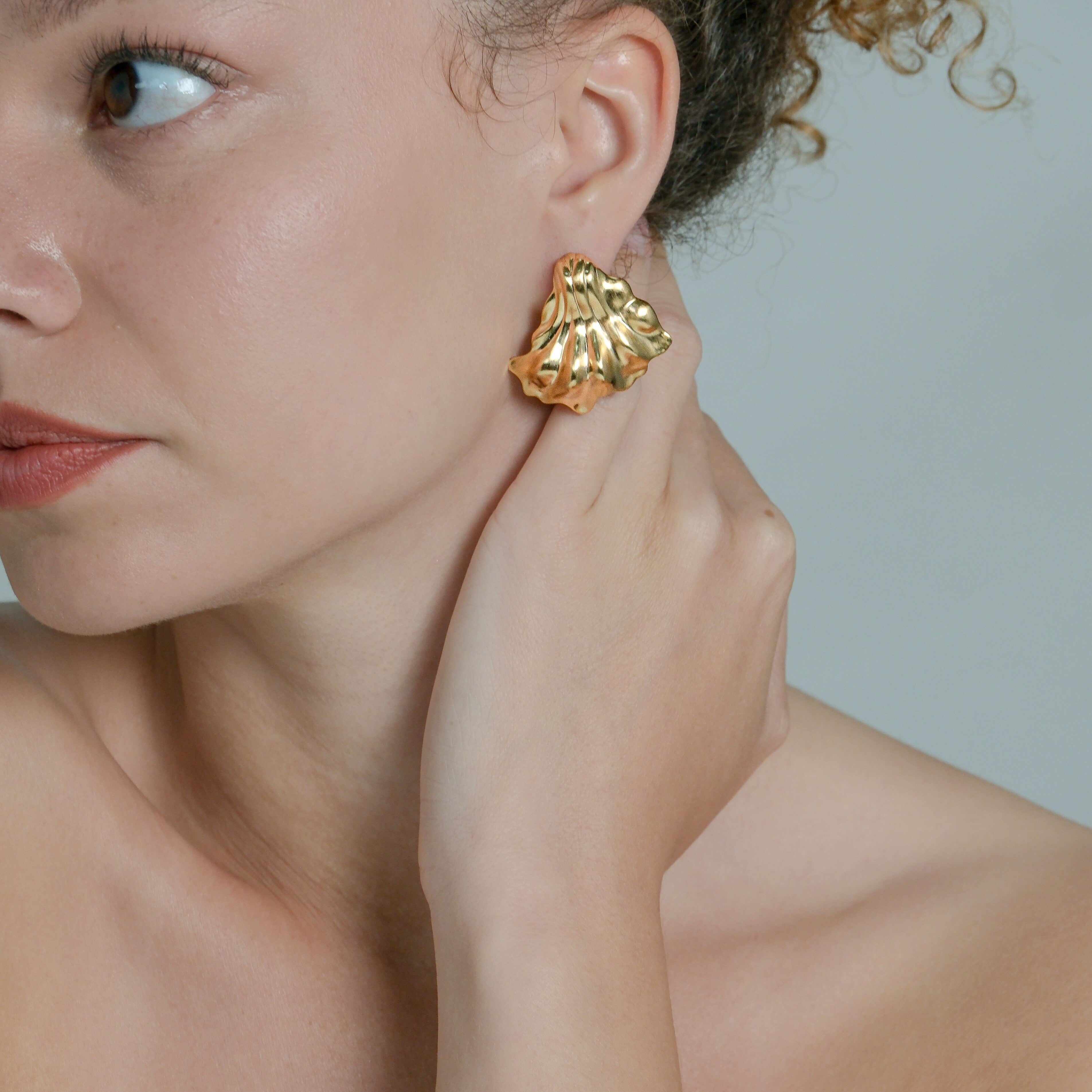 Woman wearing gold earrings against a neutral background