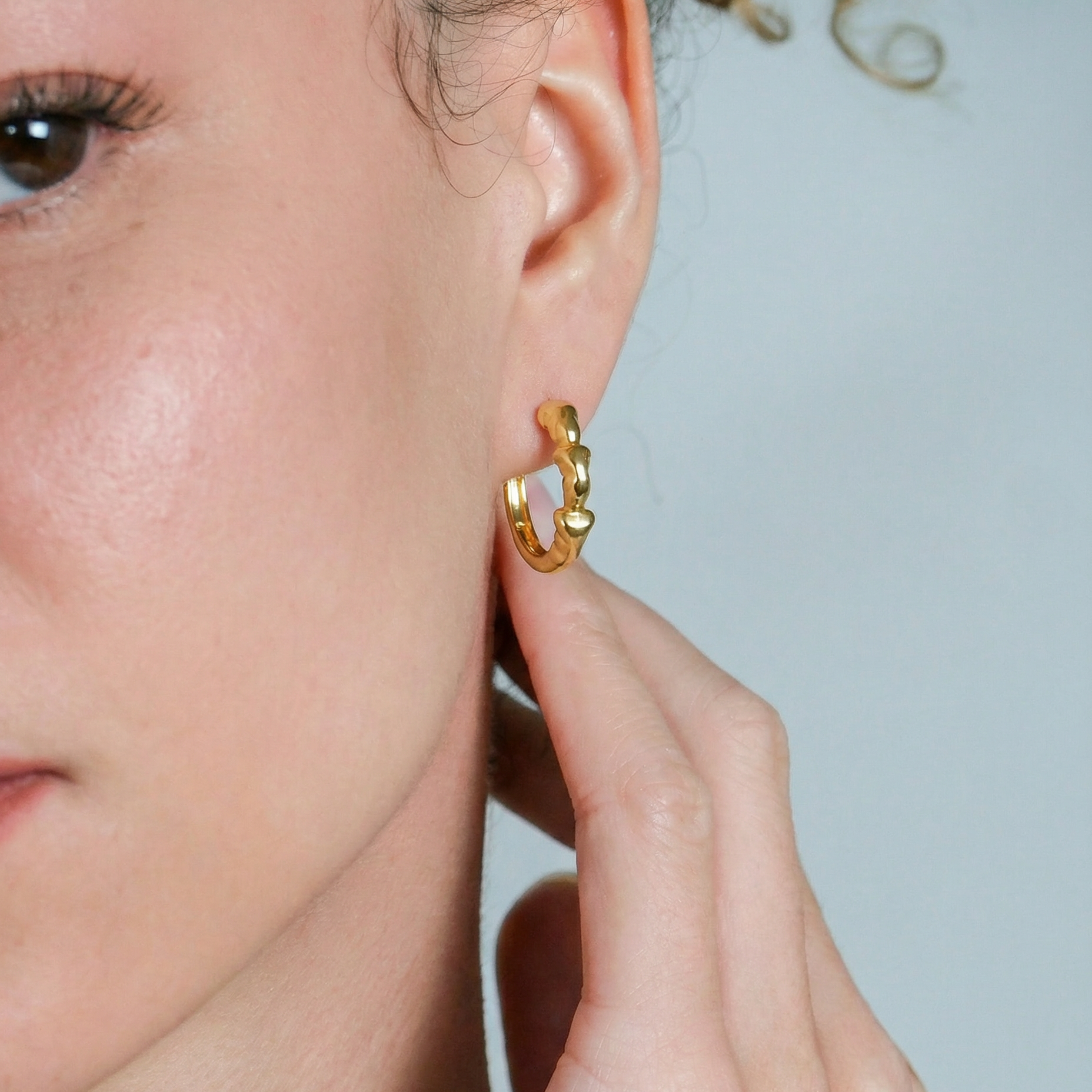 Gold hoop earring worn by a person against a neutral background