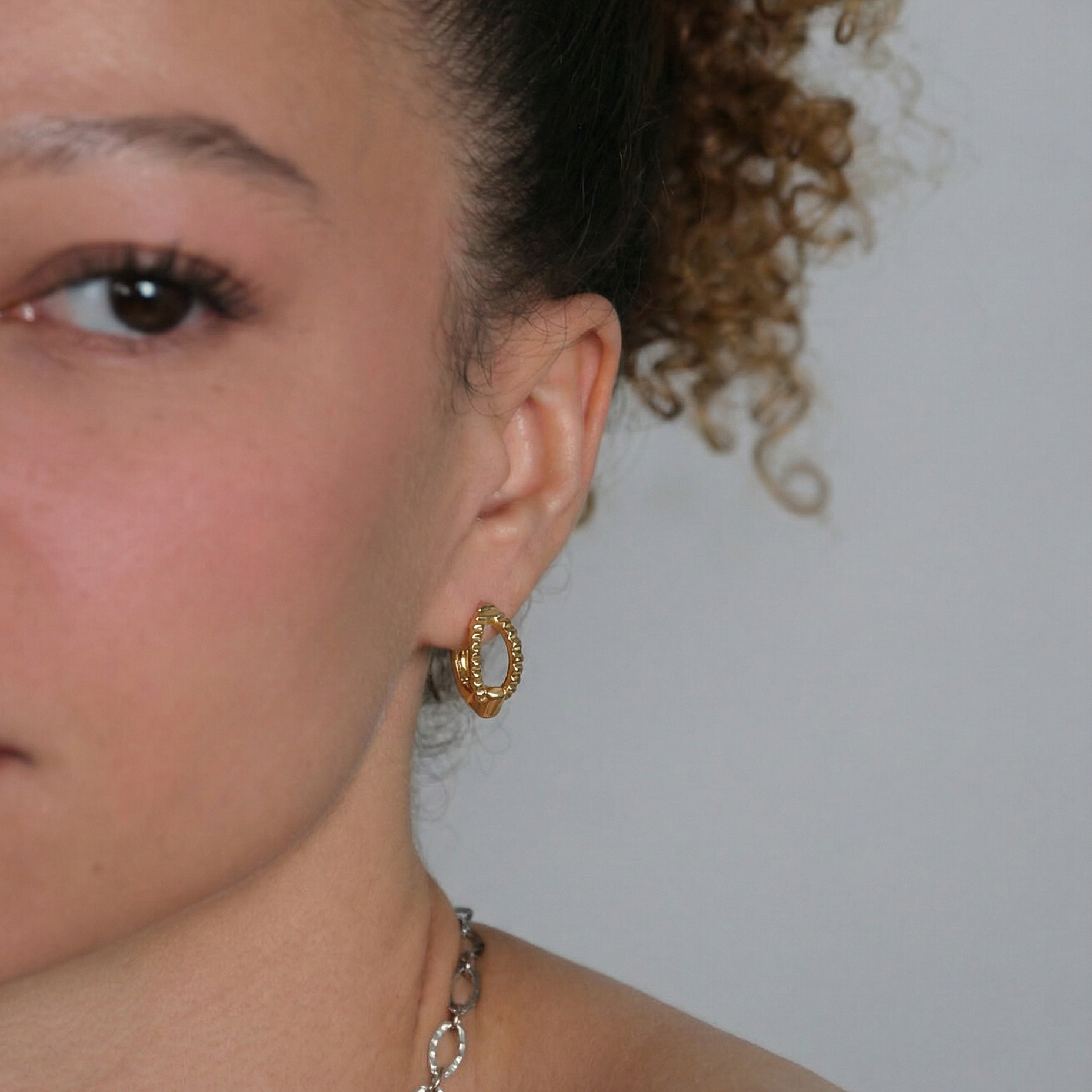 Close-up of a person wearing gold hoop earrings with a plain background