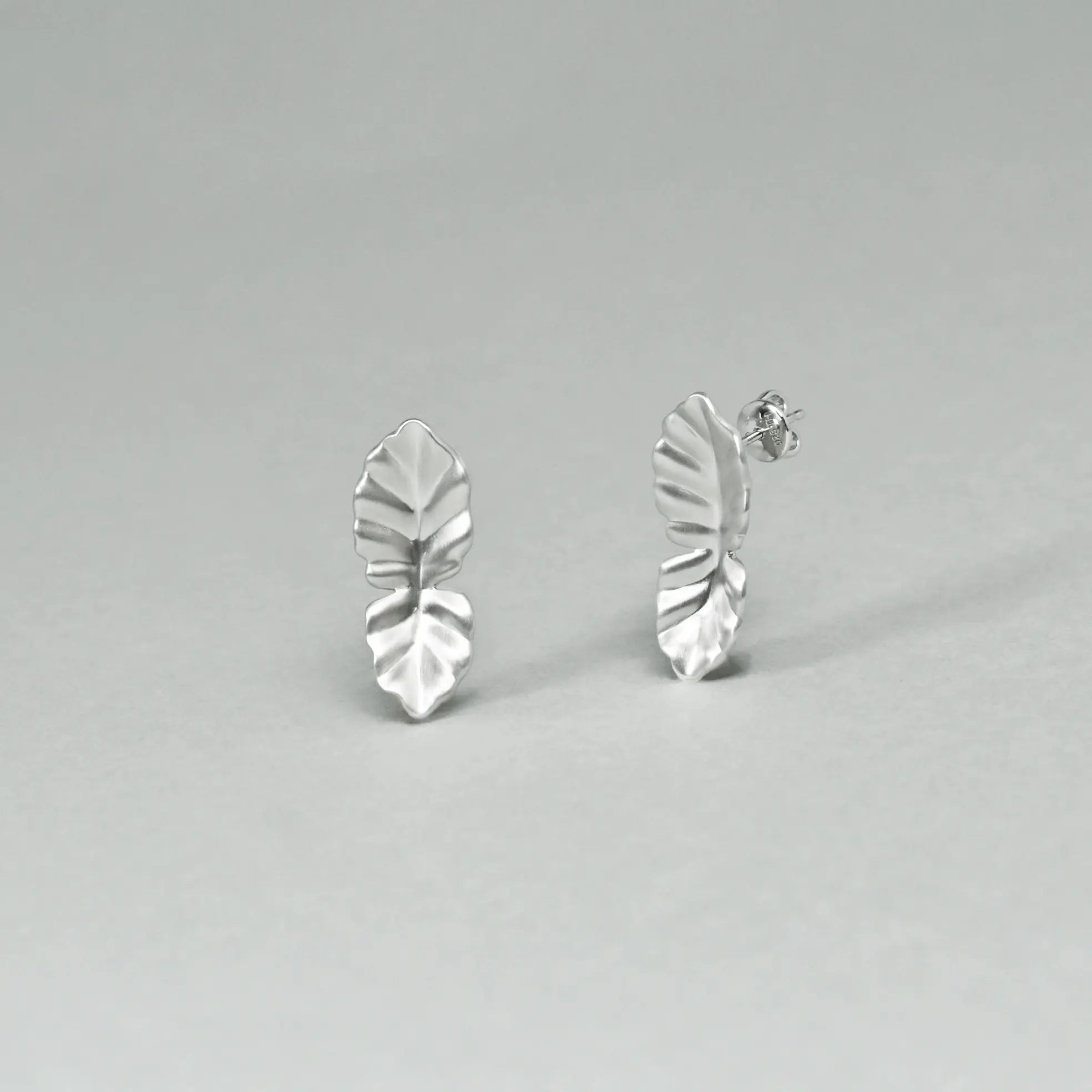 Silver leaf-shaped earrings on a gray background