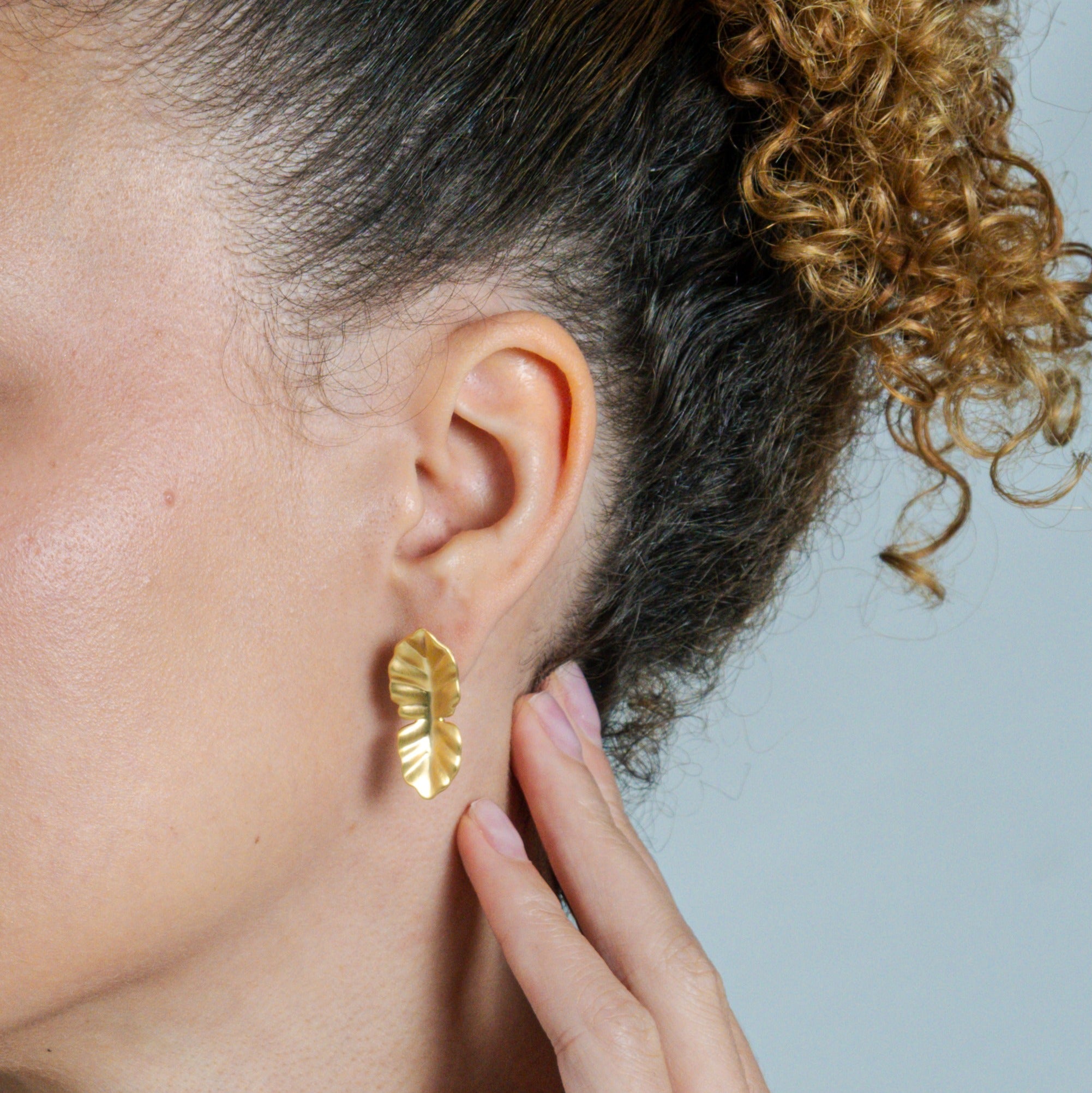 Close-up of a person wearing gold leaf earrings with a neutral background
