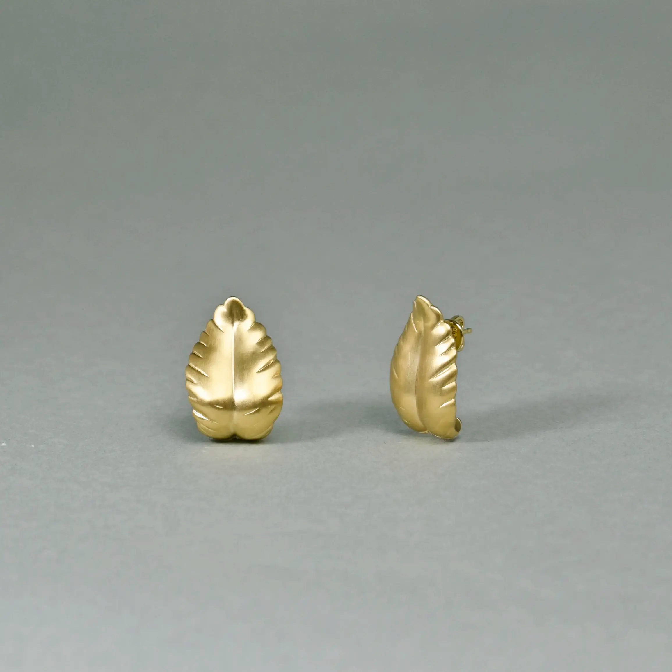 Pair of gold leaf-shaped earrings on a gray background