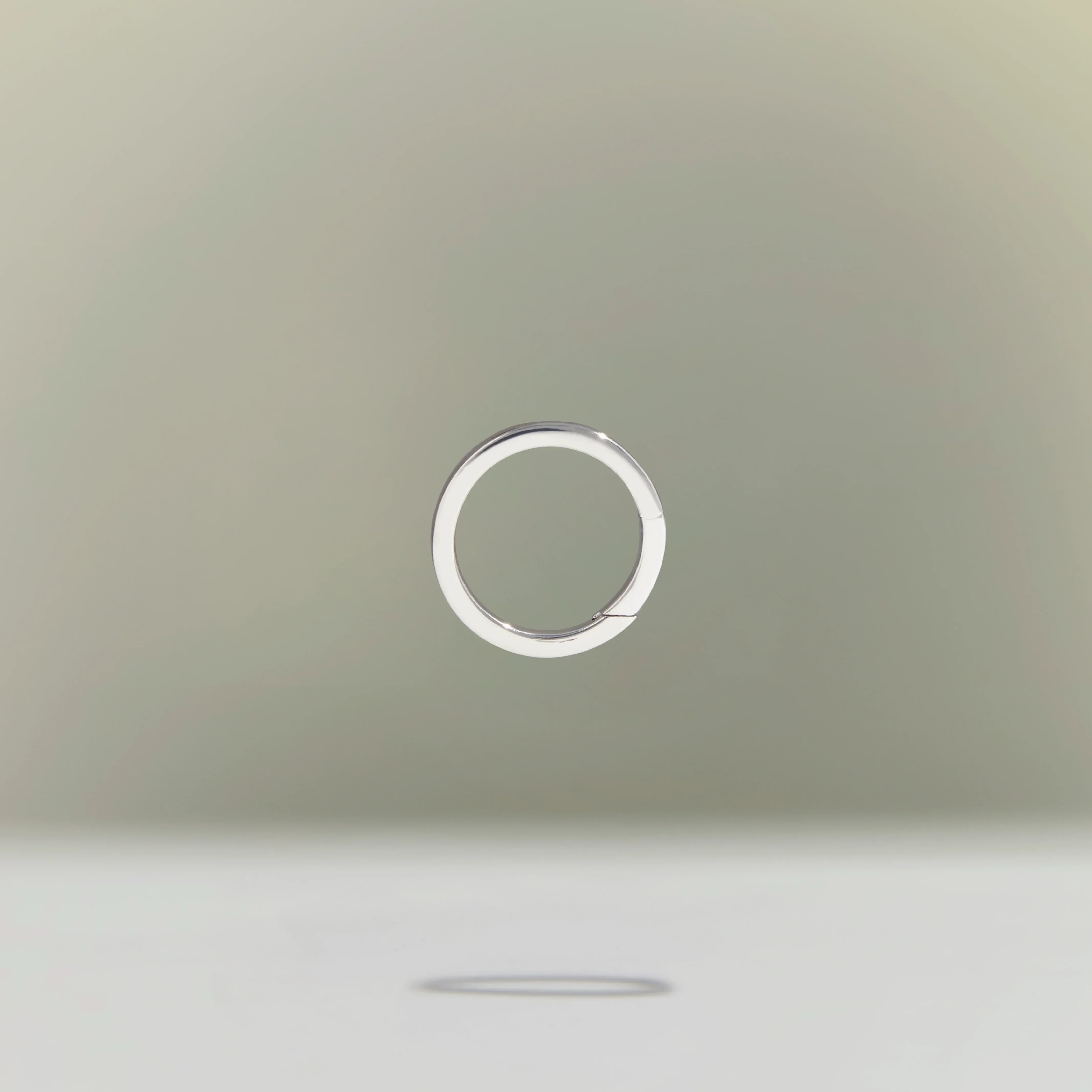 Minimalist silver circular ring floating above a neutral background.