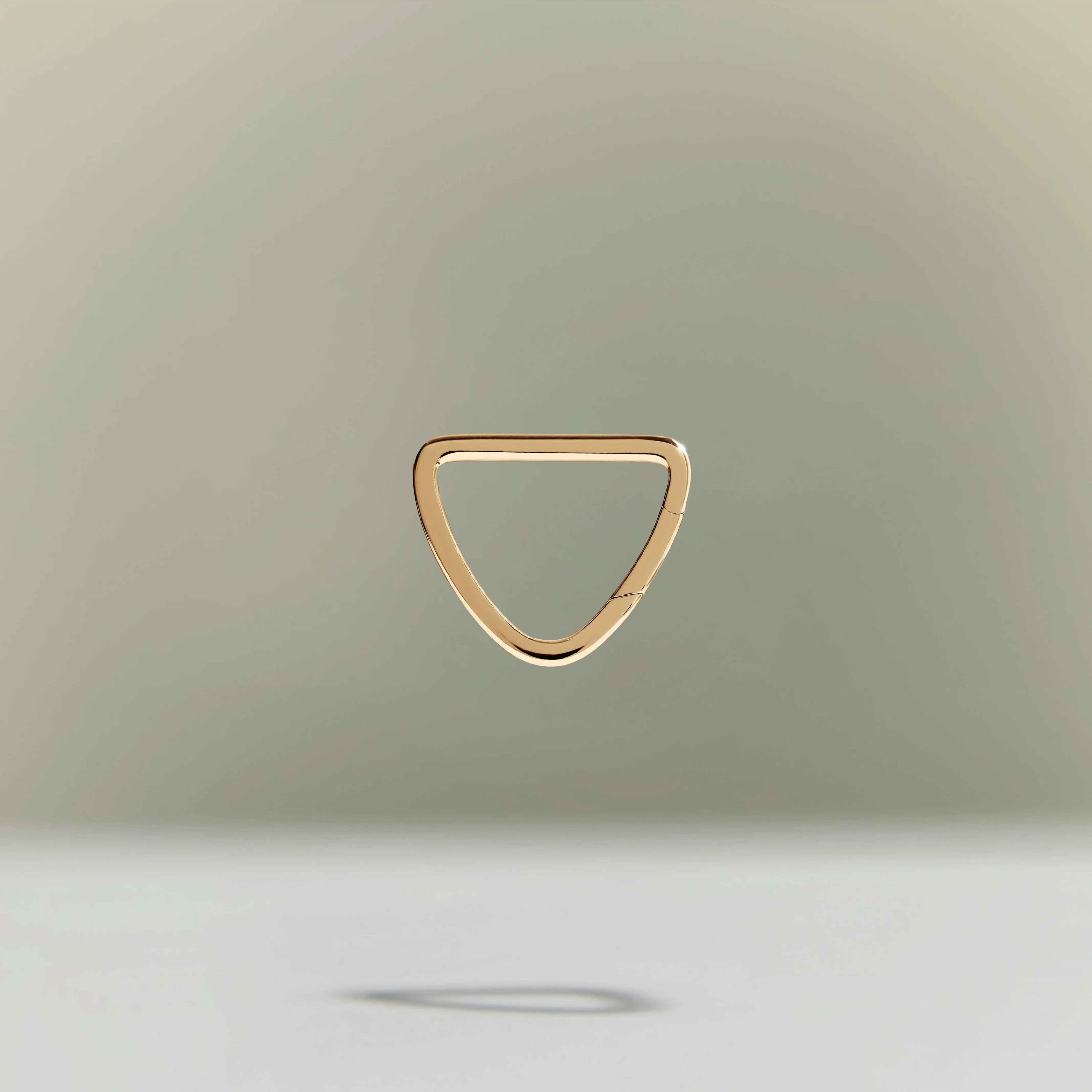 Minimalist gold triangular ring floating above a neutral background.