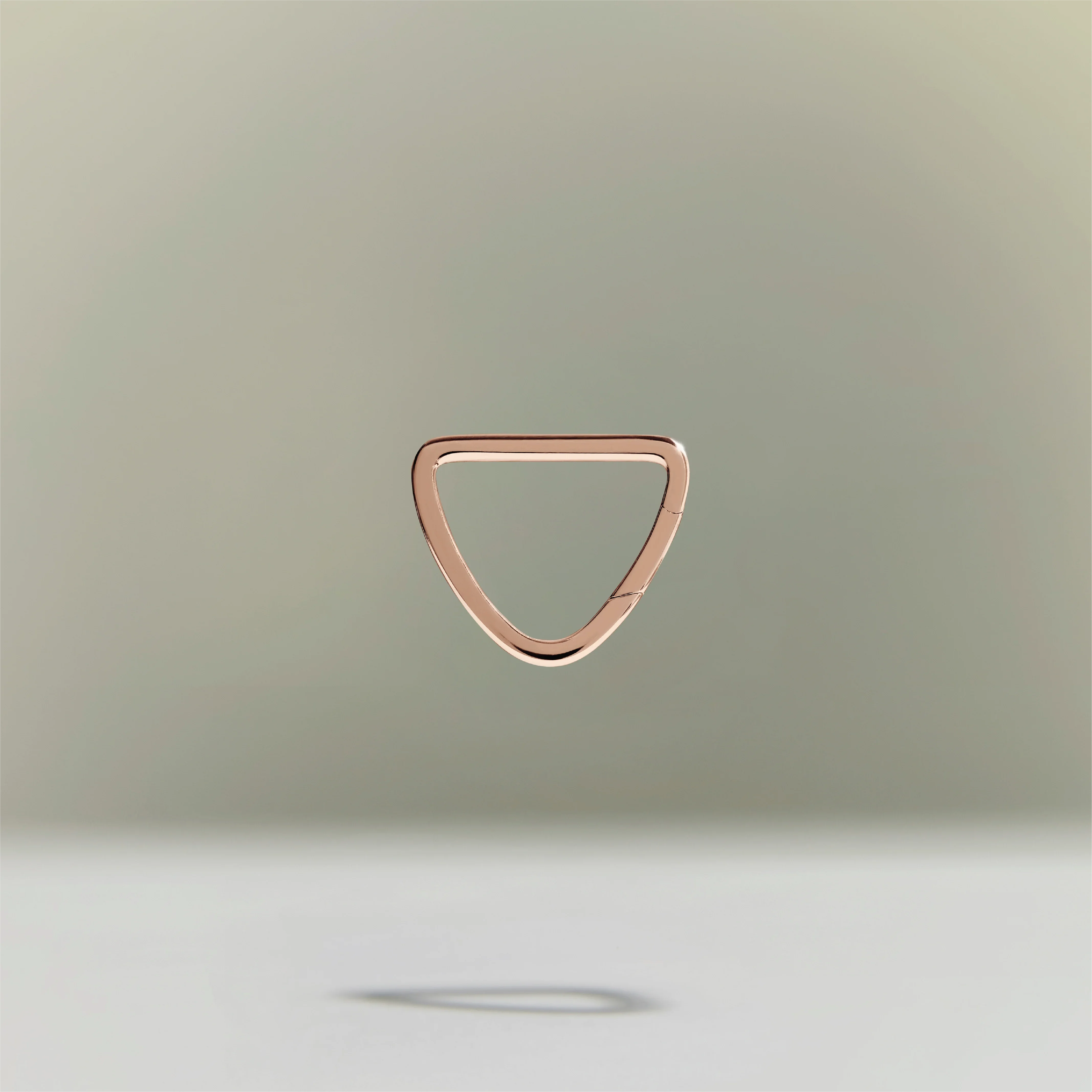 Minimalist rose gold triangular ring floating above a neutral background.