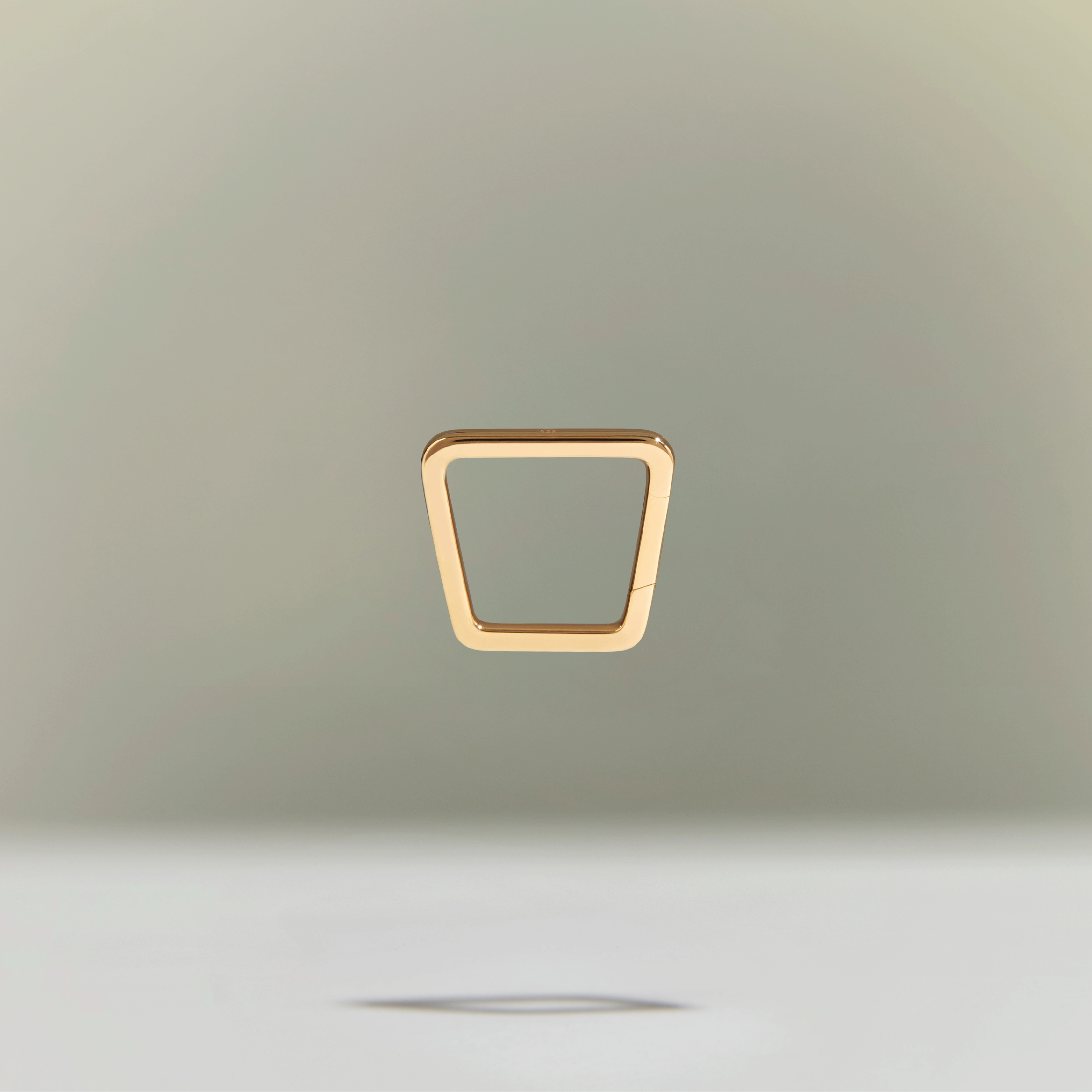 Minimalist gold trapezoid-shaped ring floating above a neutral background.