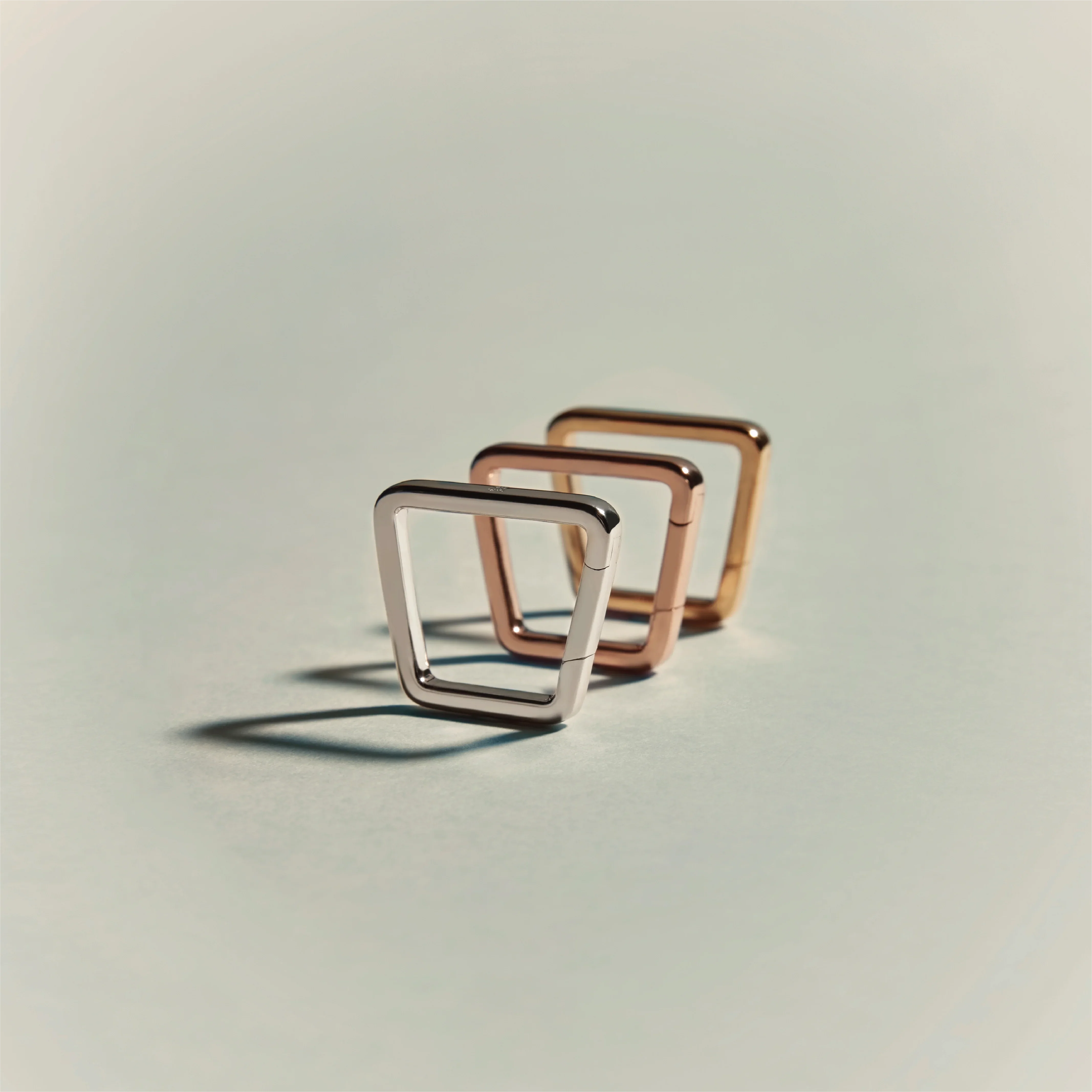 Three geometric trapezoid-shaped rings in silver, rose gold, and yellow gold arranged in a row.