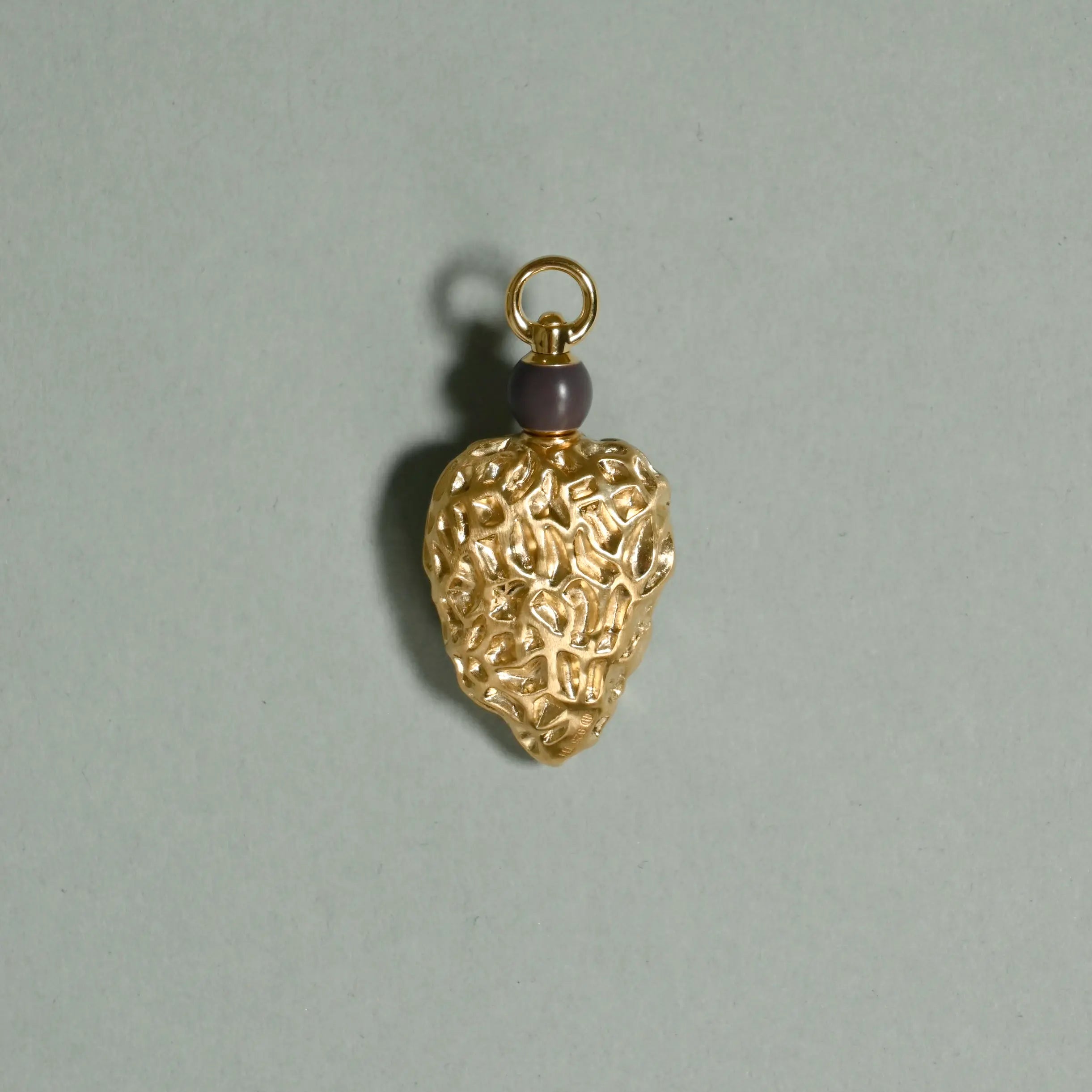 Gold pendant with intricate design on a gray background