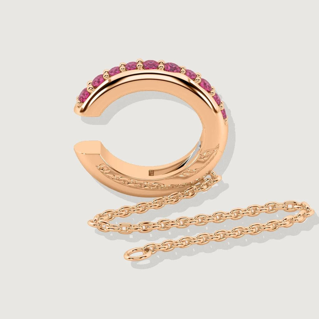 Product shot of rose gold ear cuff with row of pink gemstones and attached chain on neutral background.