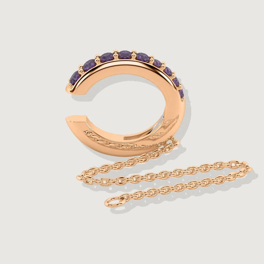 Product shot of rose gold ear cuff with row of purple gemstones and attached chain on neutral background.