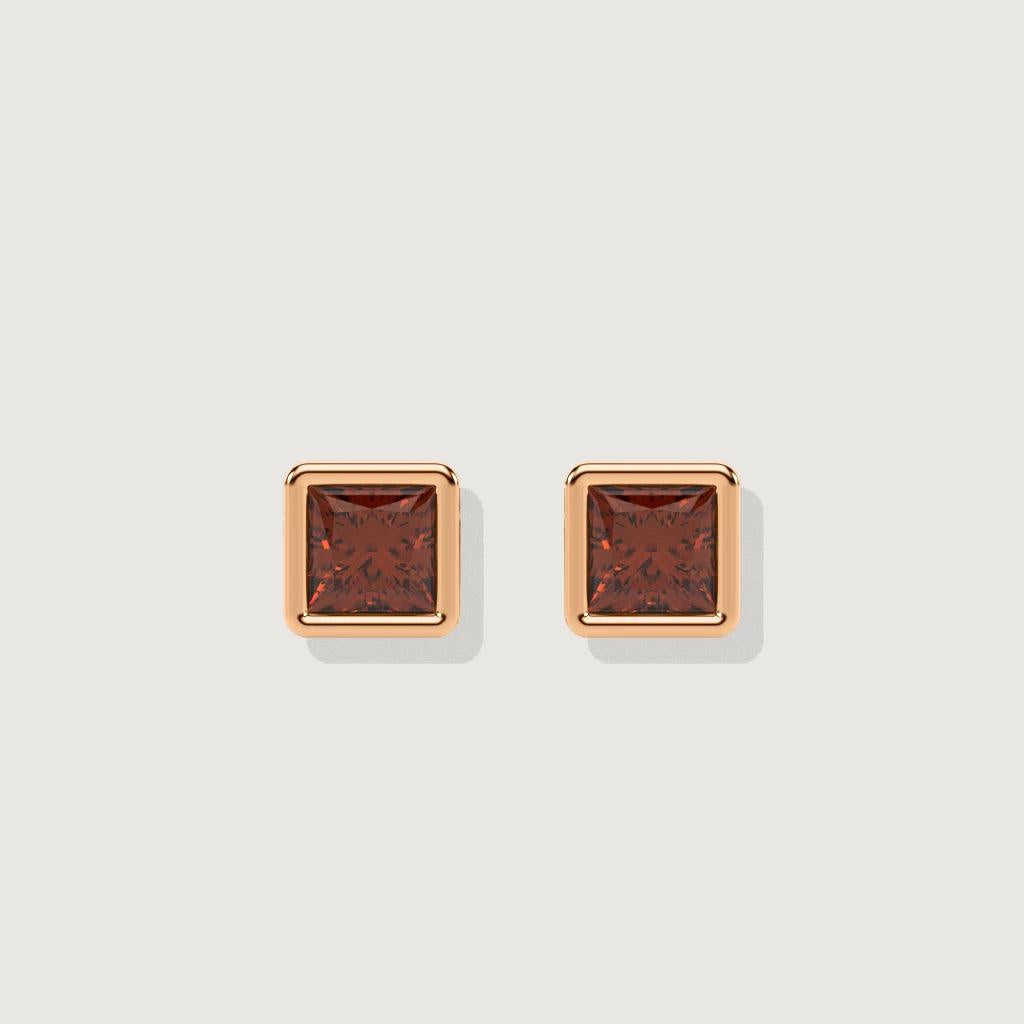 Studio product shot on a light background of a pair of polished rose gold square stud earrings set with deep ruby-red stones framed in shiny metal, designed for a sleek and modern look.