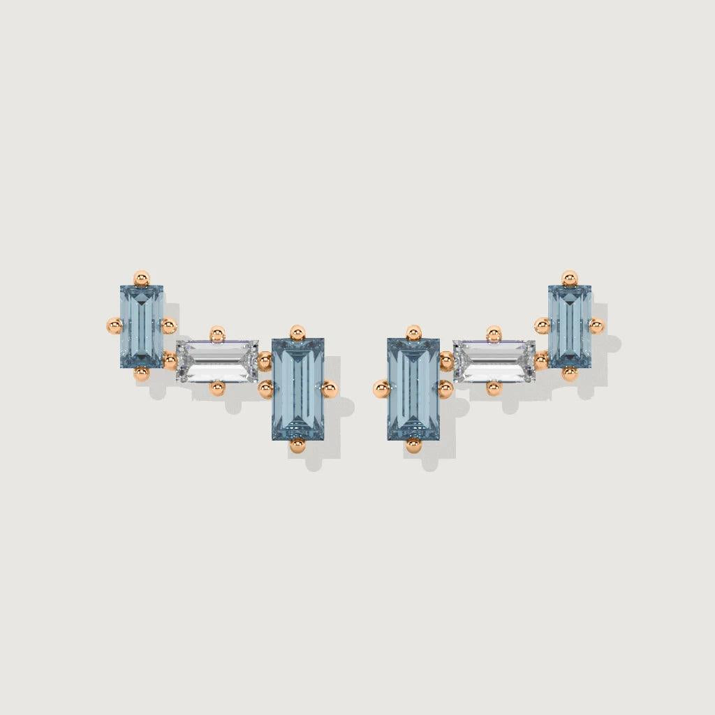 Rose gold ear crawler with baguette-cut blue topaz and white topaz stones on white background