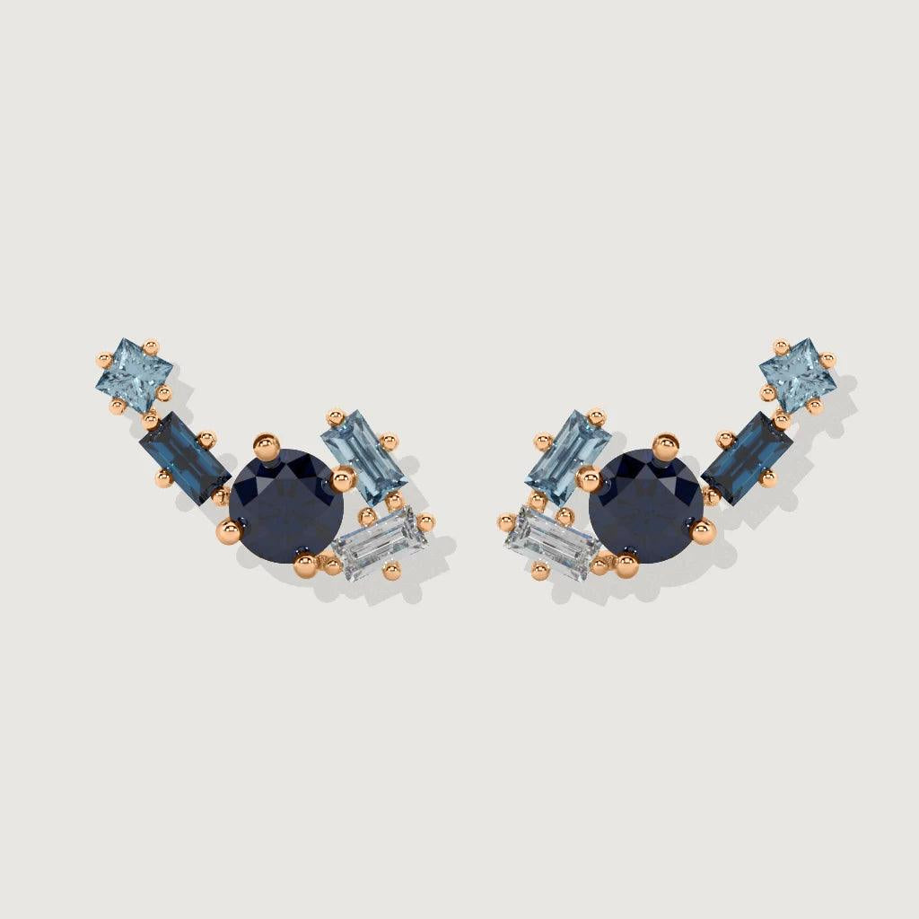 Product shot of matching pair of blue gemstone cluster ear climbers with round and baguette-cut blue stones in rose gold setting.